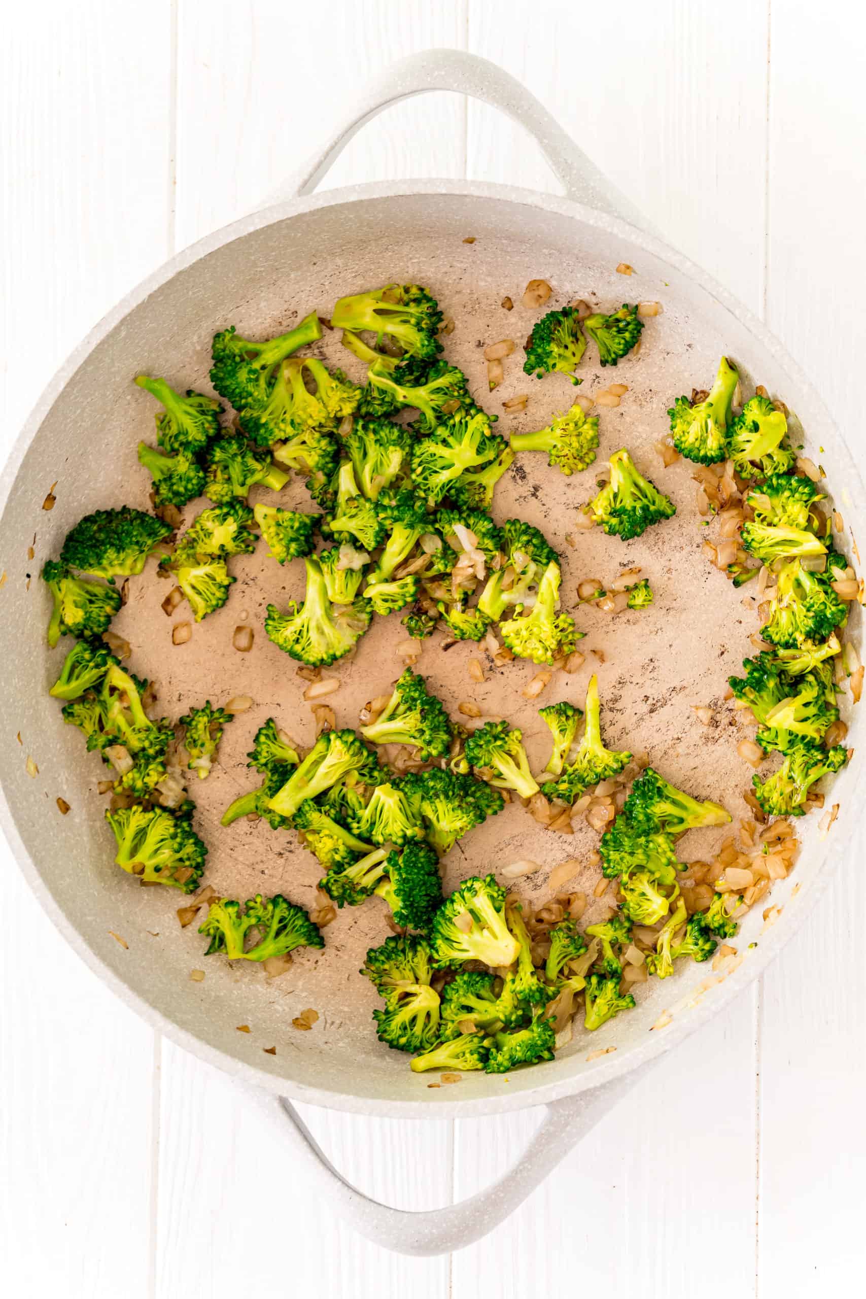 broccoli florets added to onions and oil in saute pan.