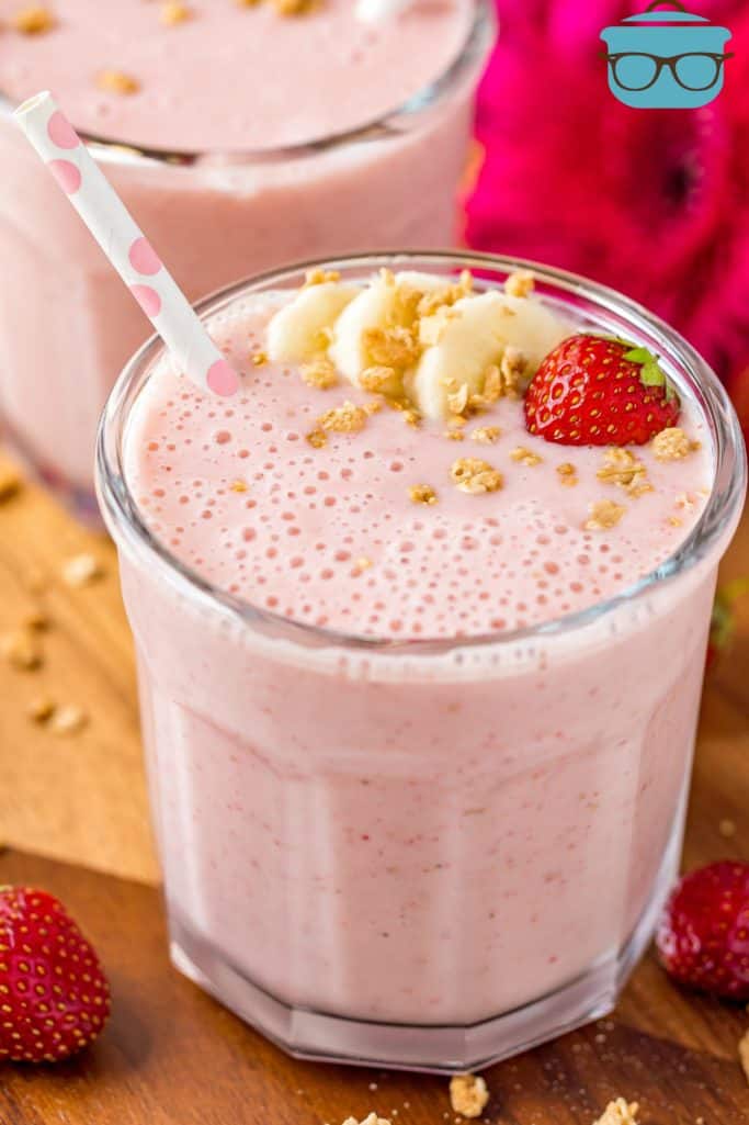 glass filled with pink smoothie and topped with sliced bananas and a fresh strawberry