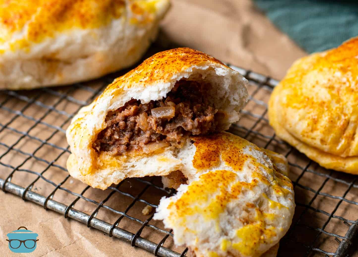 Beef and Potato Biscuit Hand Pies shown on a baking rack, one hand pie is open to show the ground beef inside.