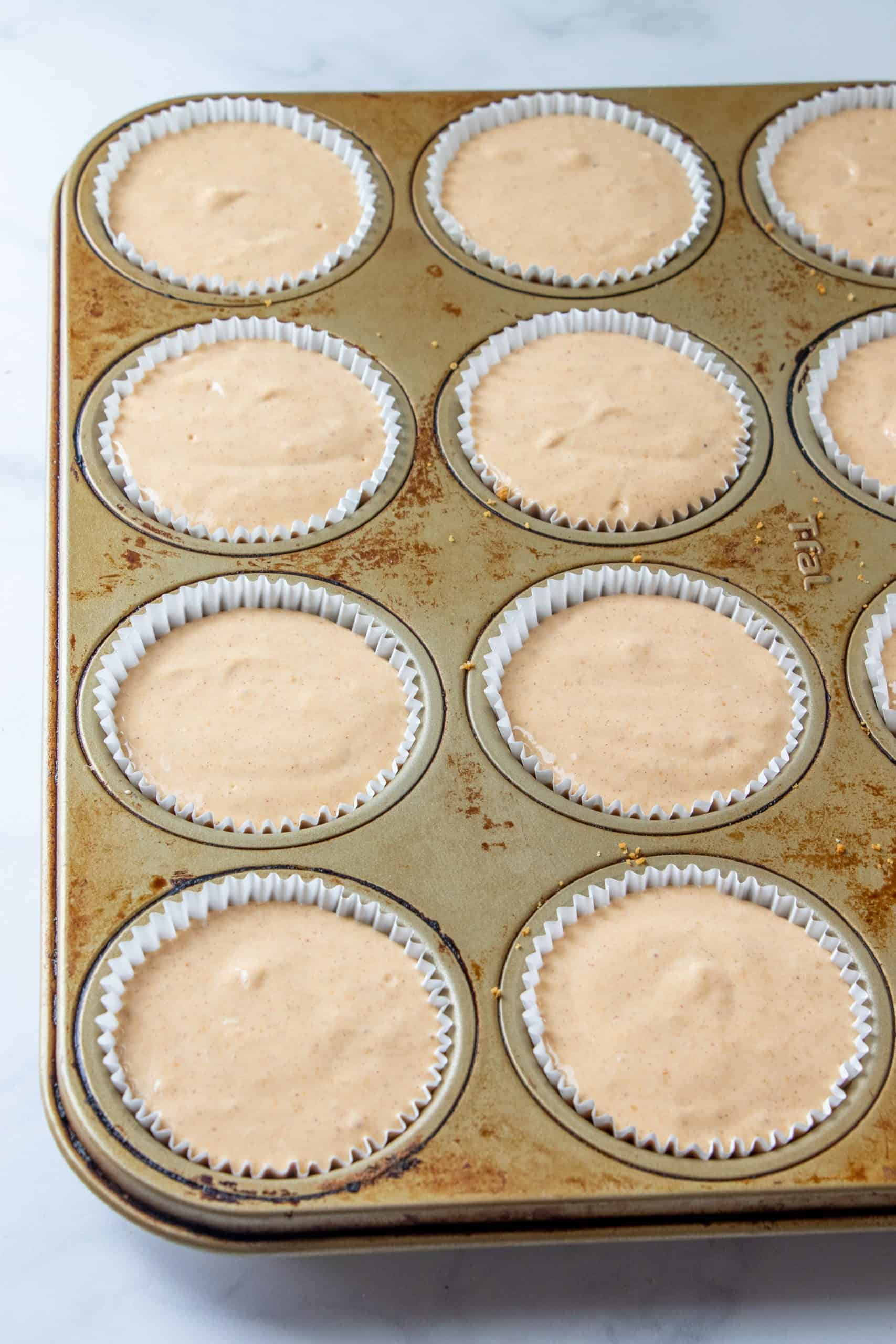 pumpkin cheesecake filling added to graham cracker crusts in a muffin pan.