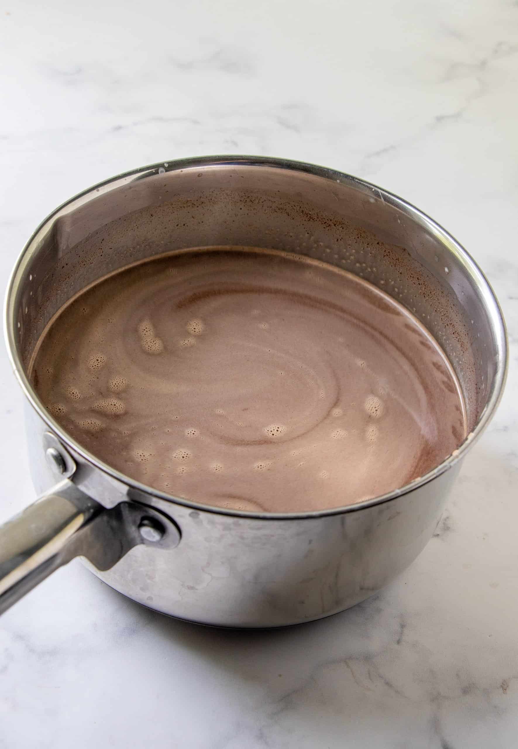 melting chocolate along with milk and sweetened condensed milk in a silver sauce pot.
