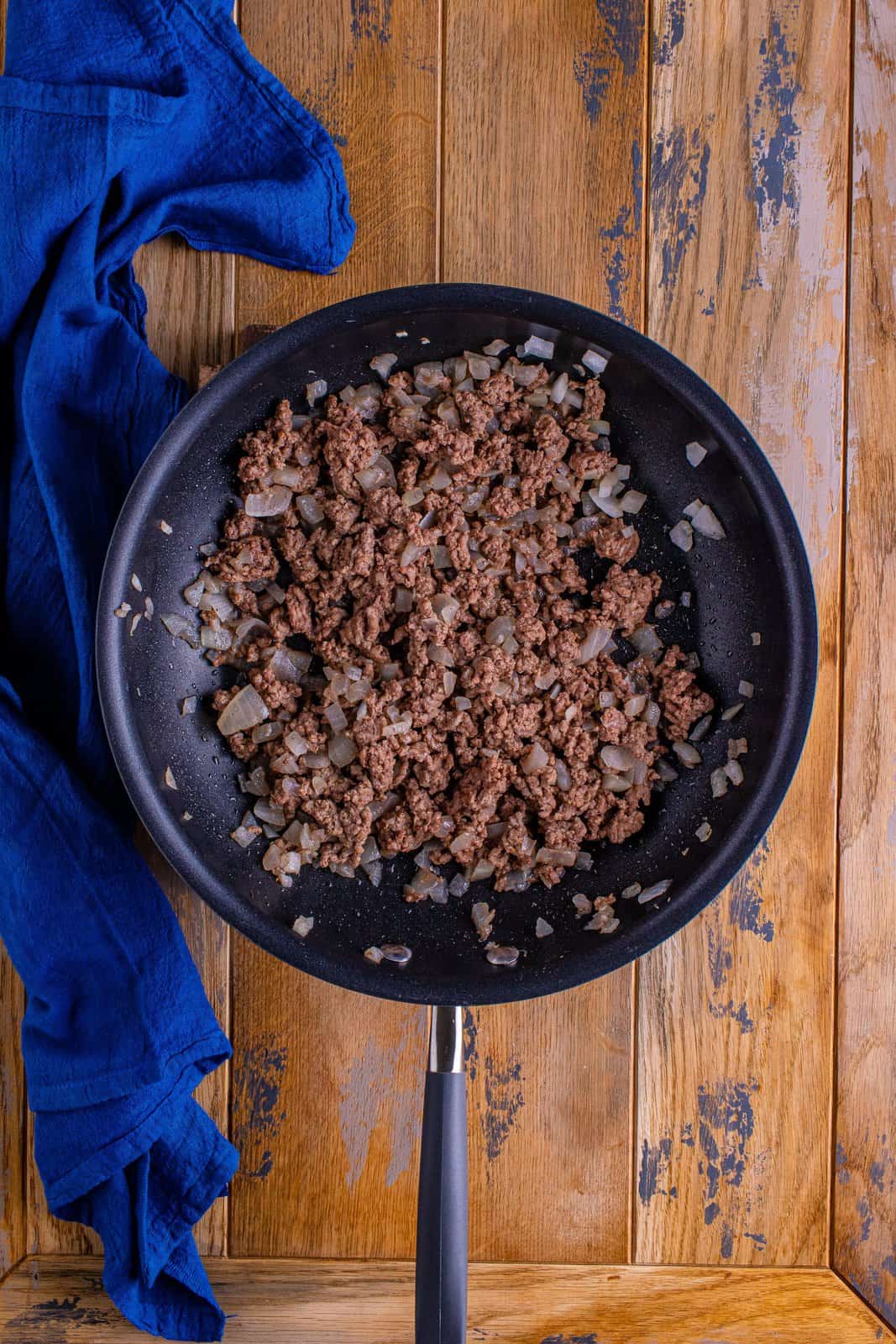 brown and crumbled ground beef along with cooked onions in a pan.