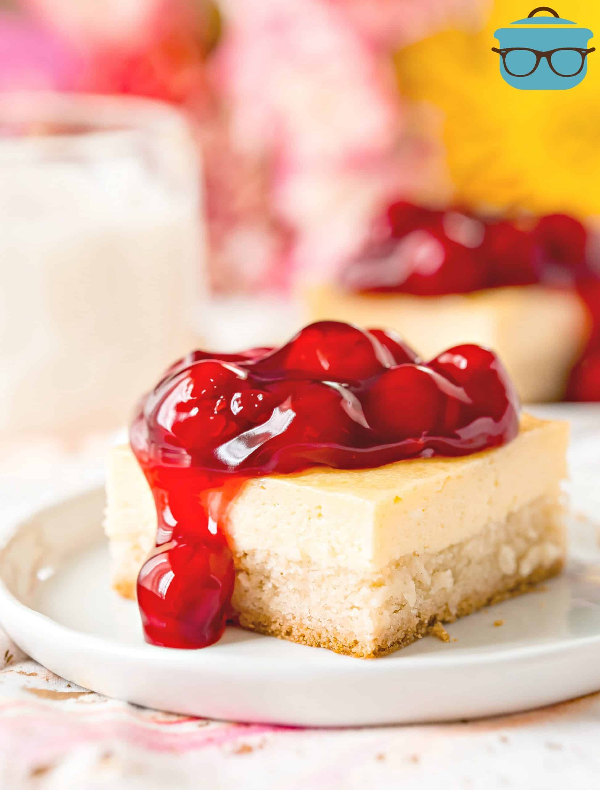 Sugar Cookie Cherry Cheesecake Bar, shown sliced on a white plate with cherry pie filling topping.