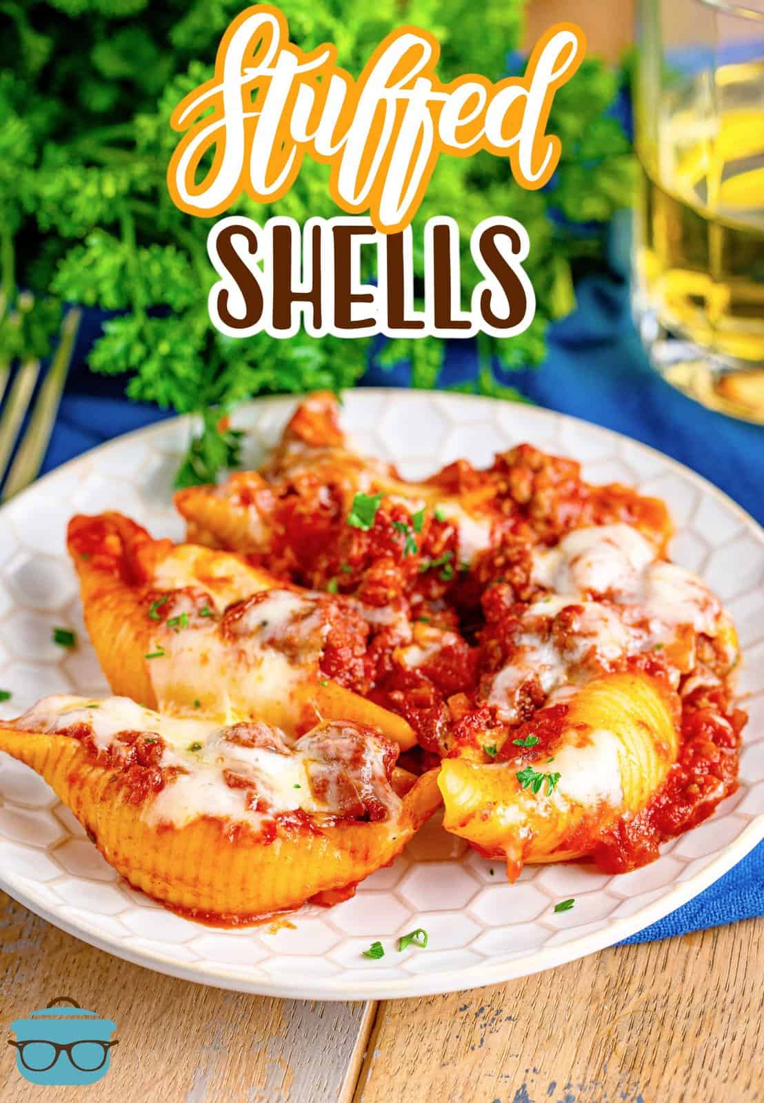 stuffed shells shown served on a small, round white plate with a glass of white wine and fresh parsley in the background.