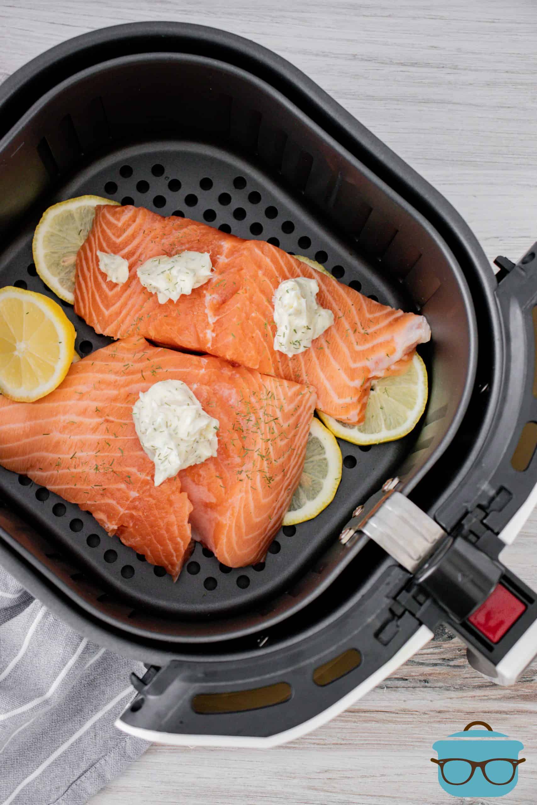 slices of fresh salmon in an air fryer basket with lemon slices and lemon garlic dill butter.