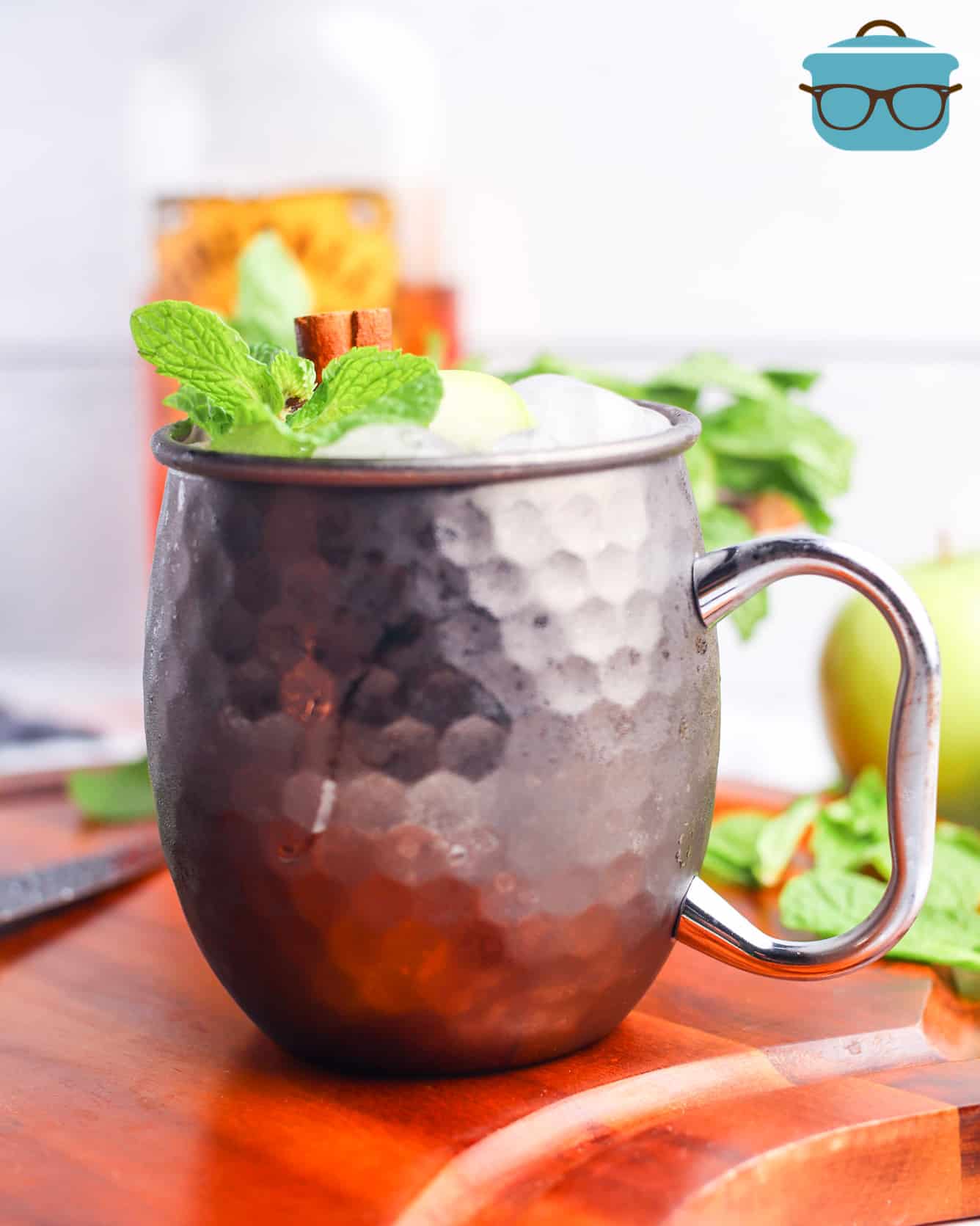 Apple Cider Moscow Mule, shown with a sprig of mint and a bottle of Fireball Cinnamon Whisky in the background.