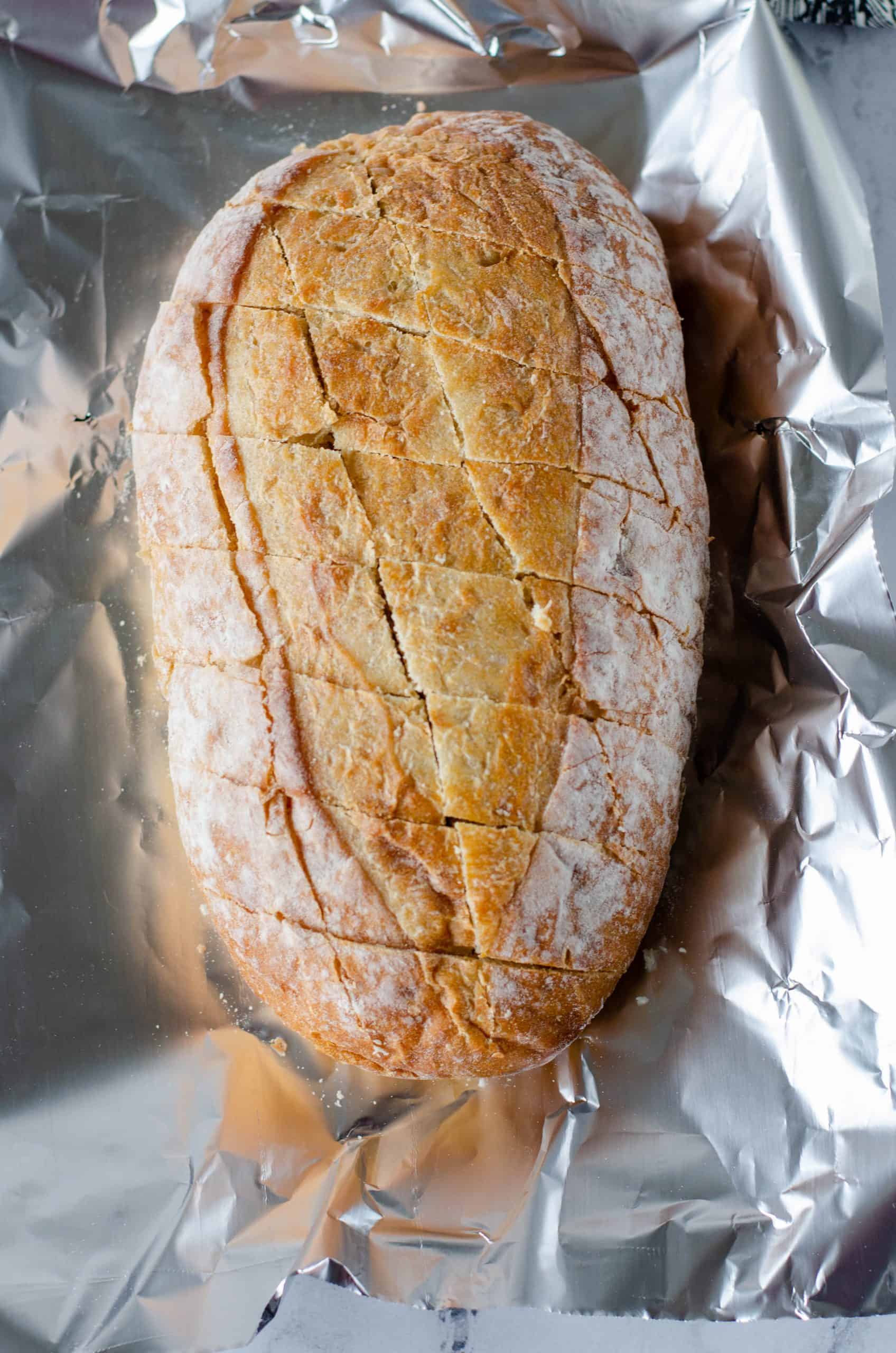 oval ciabatta loaf bread cut diagonally in two directions, bread shown on aluminum foil.