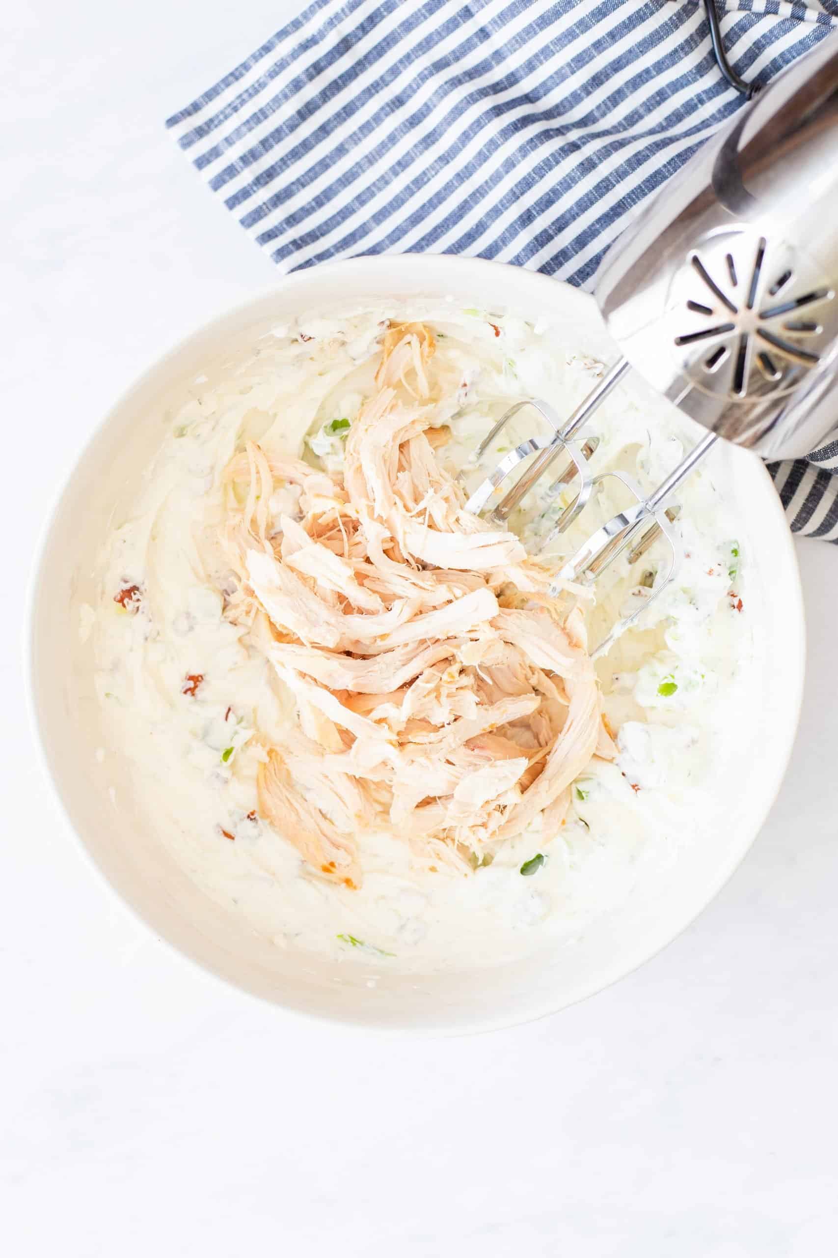 shredded chicken added to cream cheese mixture in a bowl.