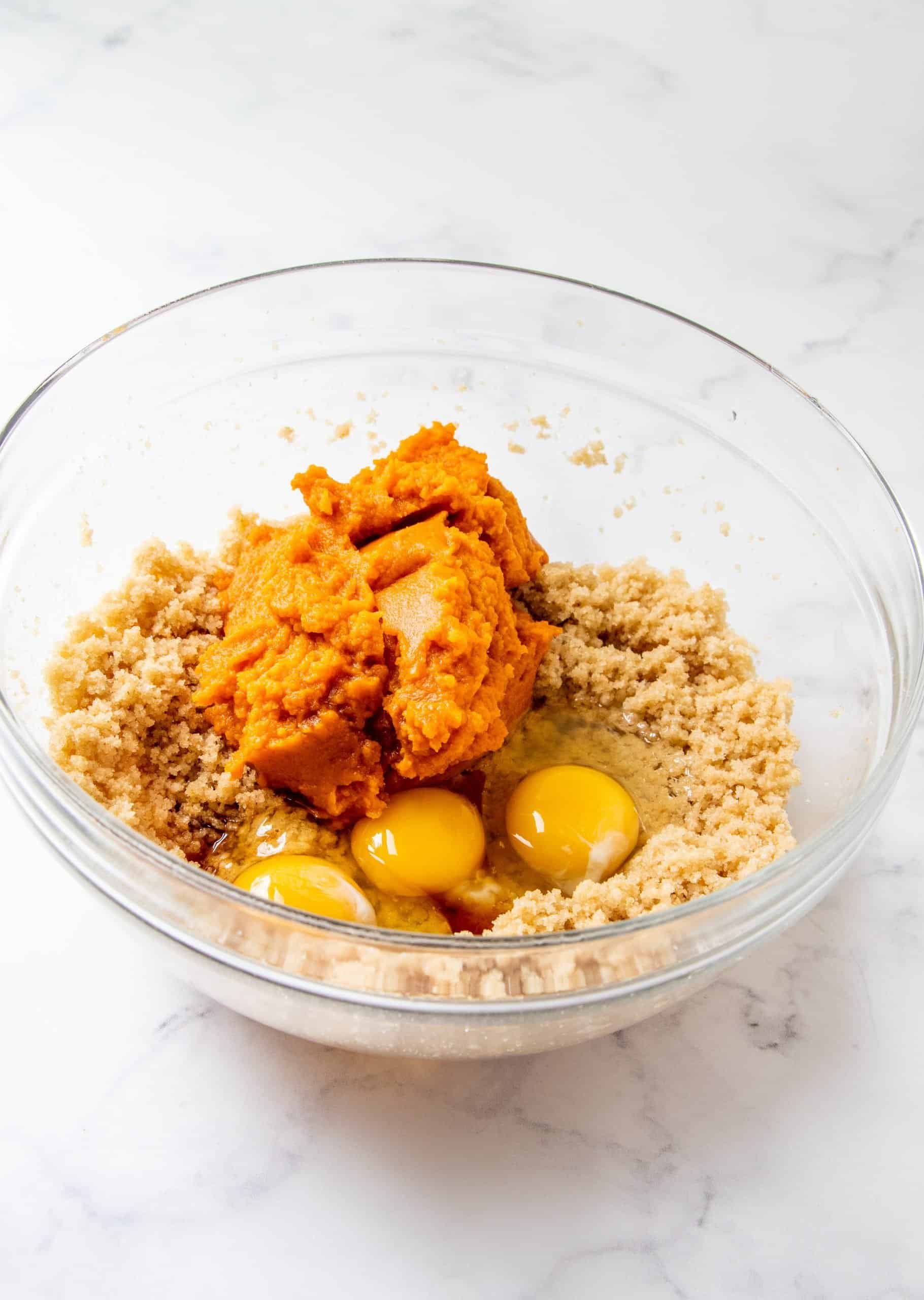 eggs and canned pumpkin added to butter and sugar mixture in a bowl.