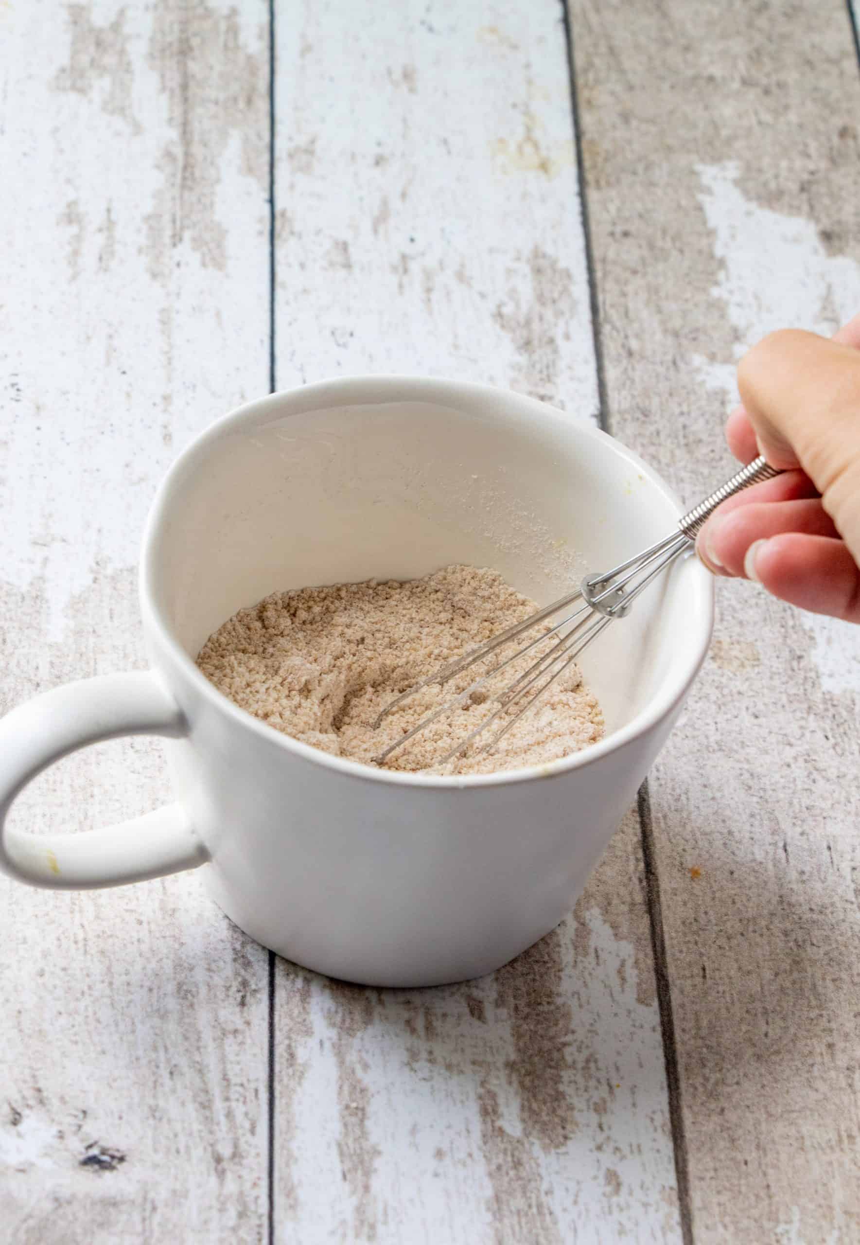 flour, sugar, baking powder, salt and pumpkin pie spice whisked together in a white mug.
