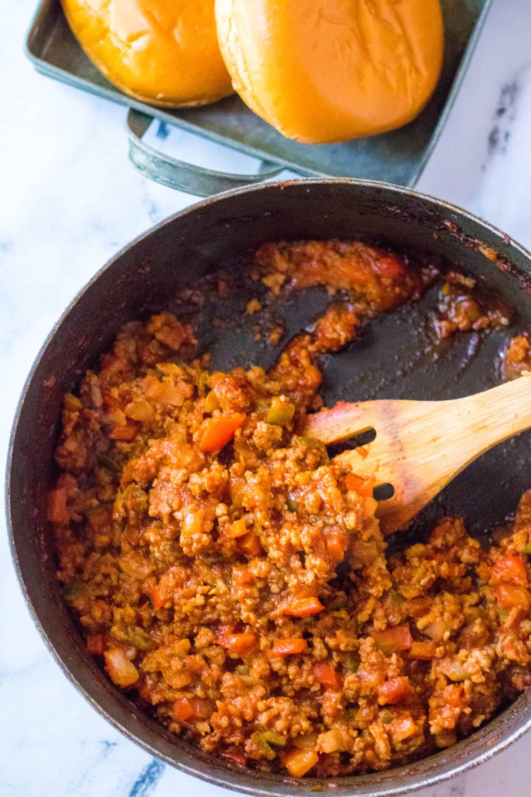 sausage and pepper sloppy Joe mixture in a large skillet stirred by a wooden spoon.