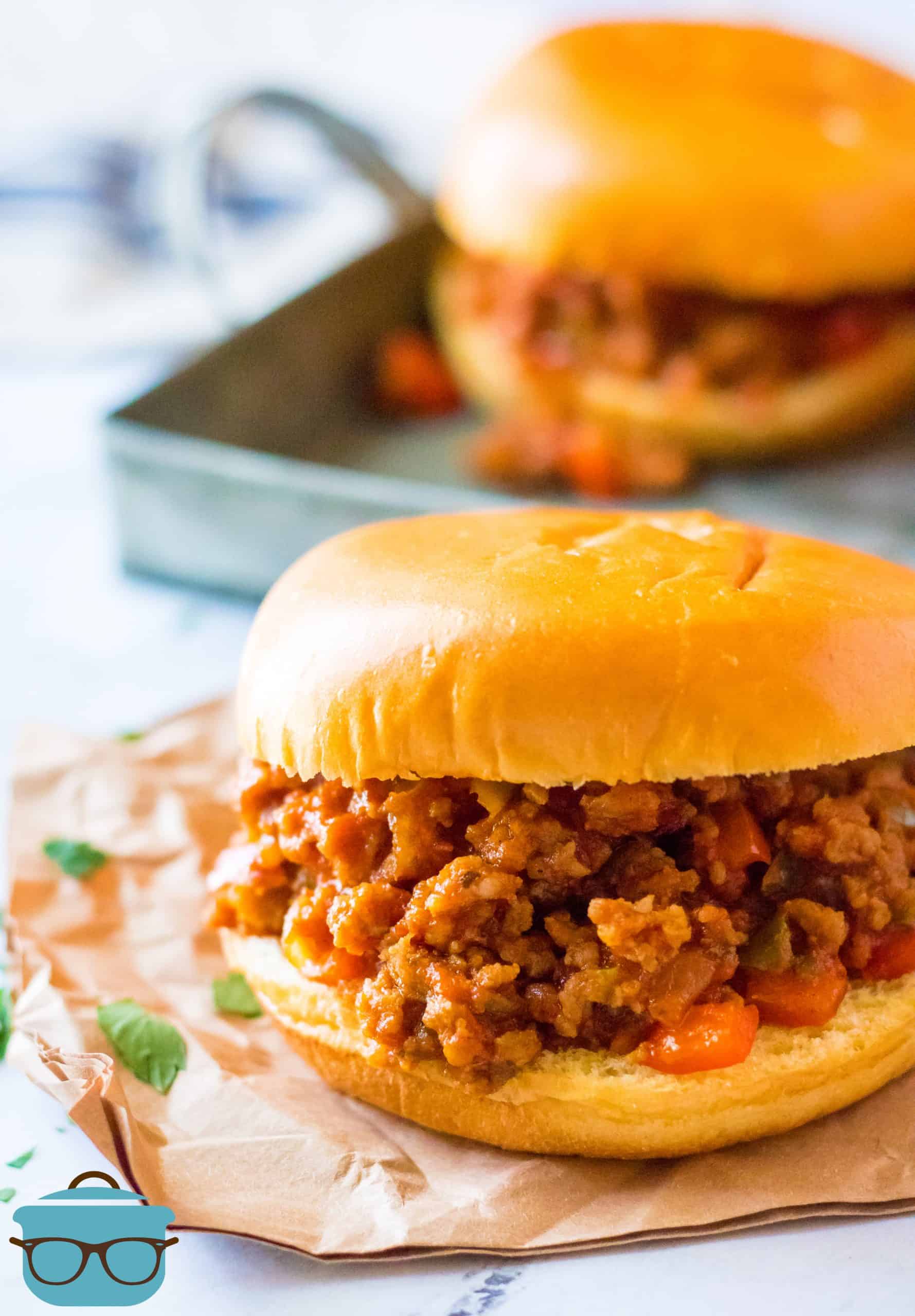 Sausage and Peppers Italian Sloppy Joes, sandwich shown on brown napkins with a sandwich in the background. 