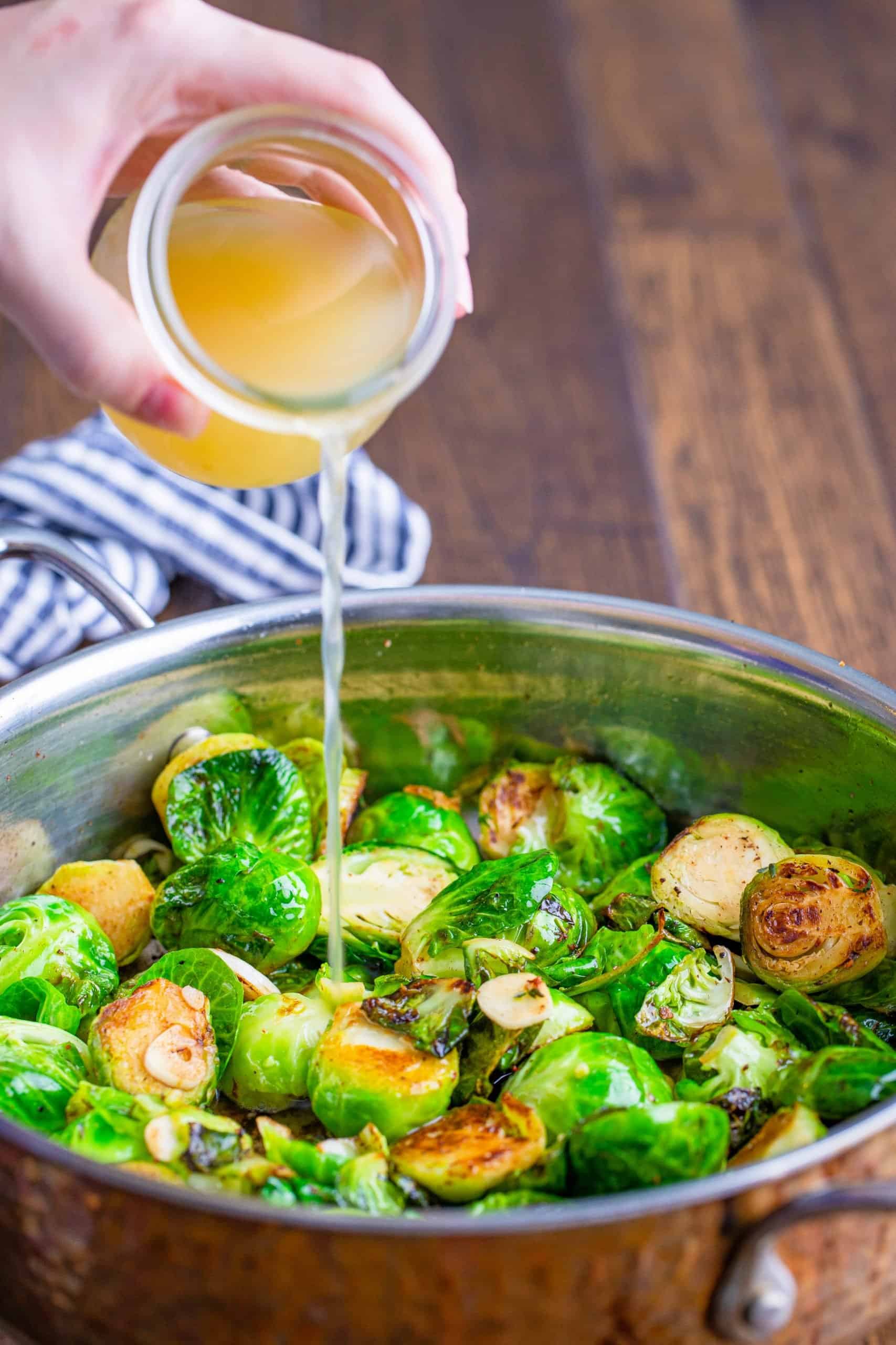 pouring chicken broth onto brussel sprouts in a pan.