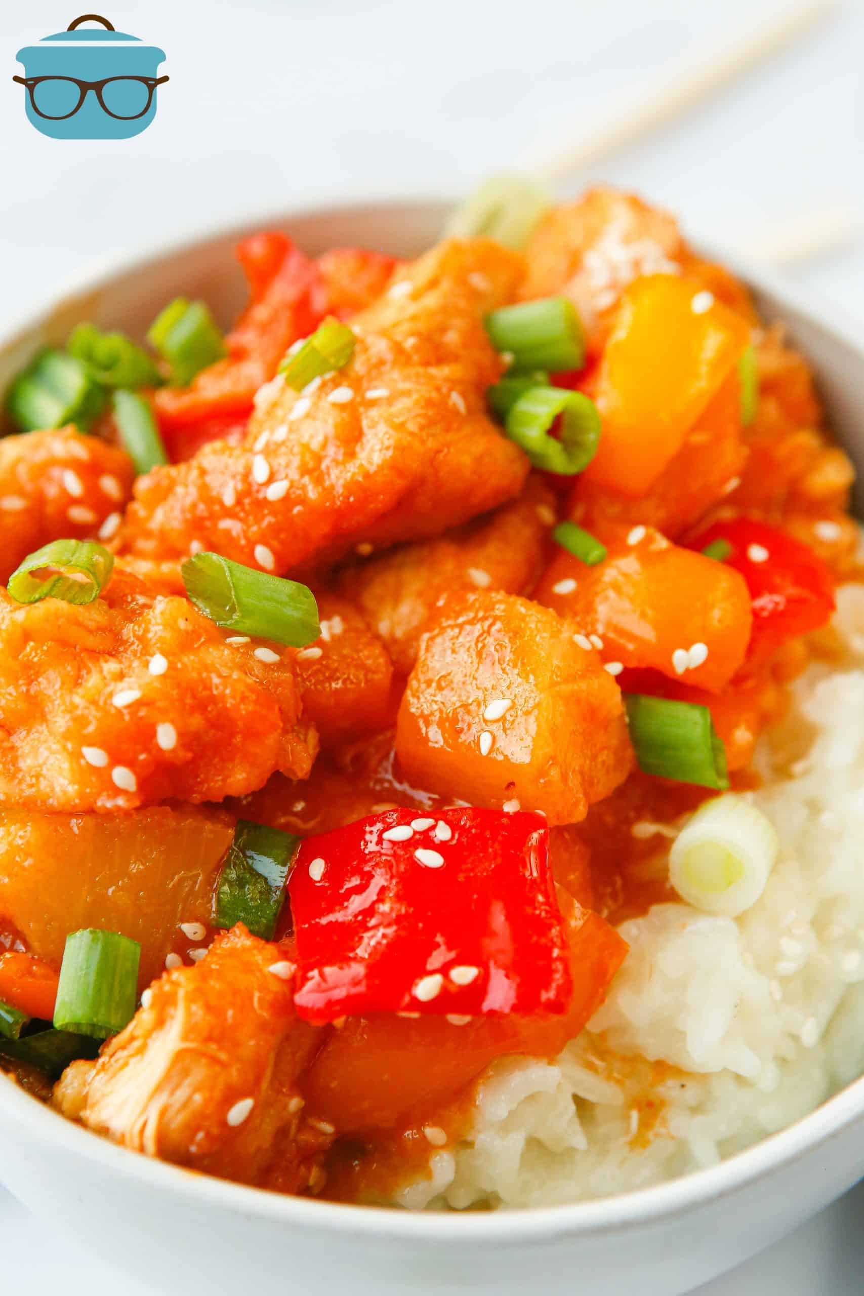 sweet and sour chicken served over rice in a bowl with chopsticks.