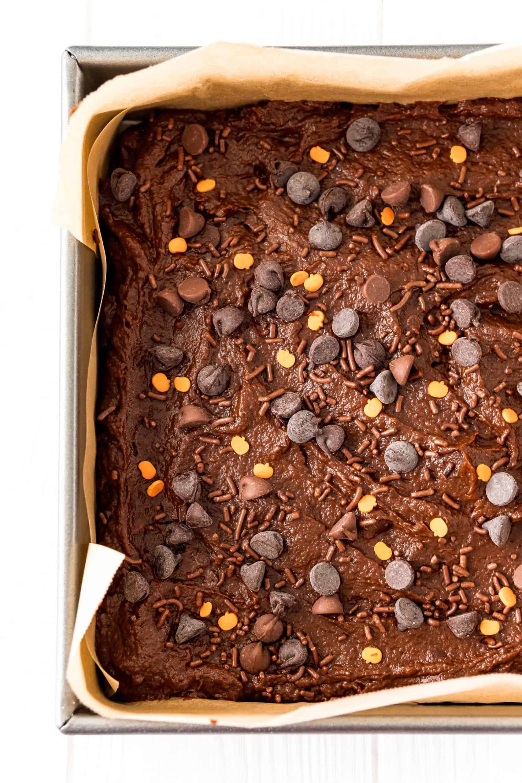 pumpkin chocolate cake batter spread into a square baking pan lined with brown parchment paper.