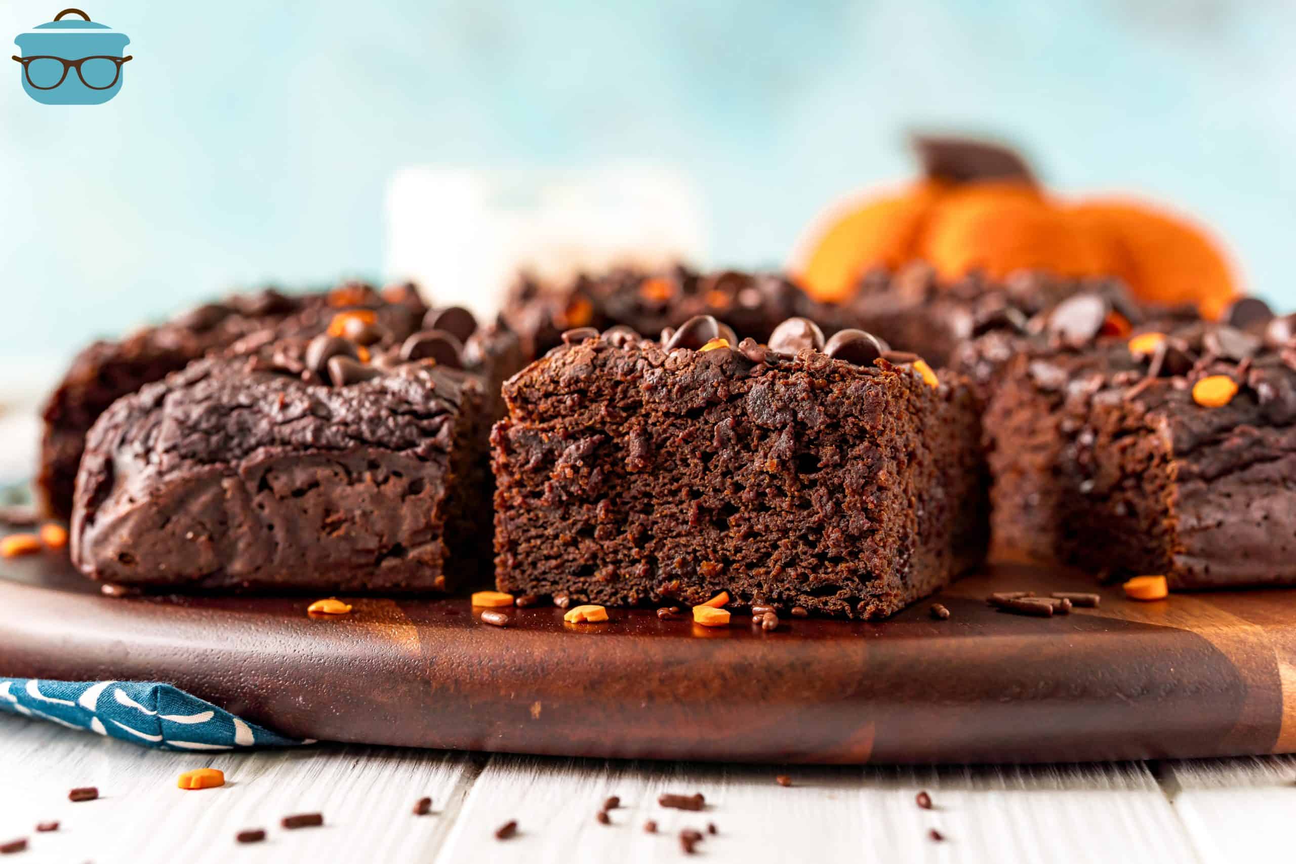 Slices of chocolate pumpkin snack cake shown on a wooden plate with a small pumpkin in the background.
