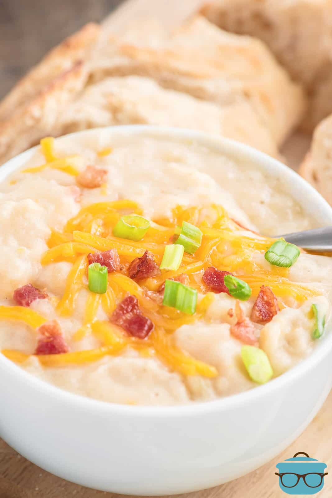 white bowl filled with potato soup and topped with cheese, bacon and sliced green onions. 