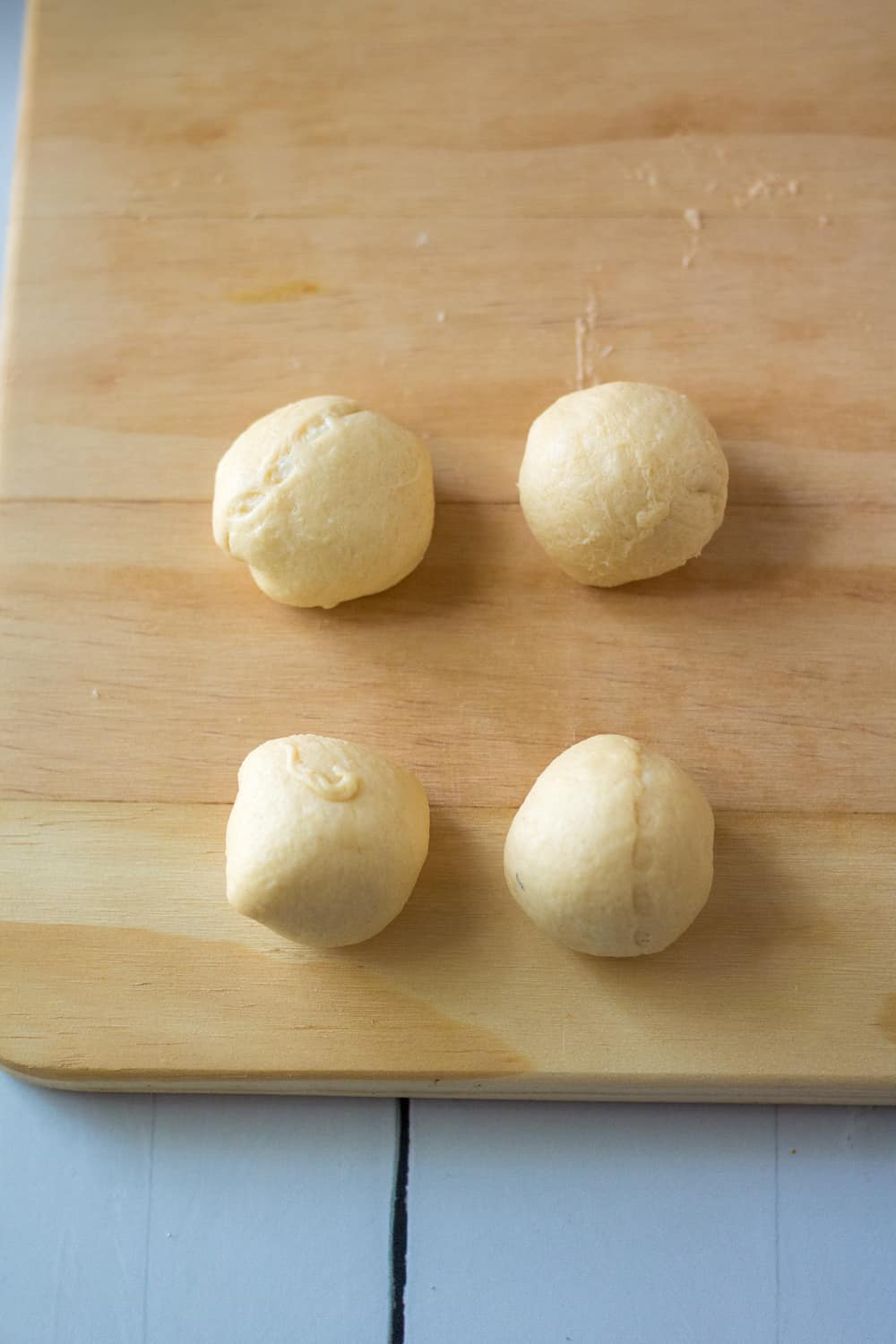 crescent roll dough wrapped around cream cheese shaped into balls on a wooden cutting board.