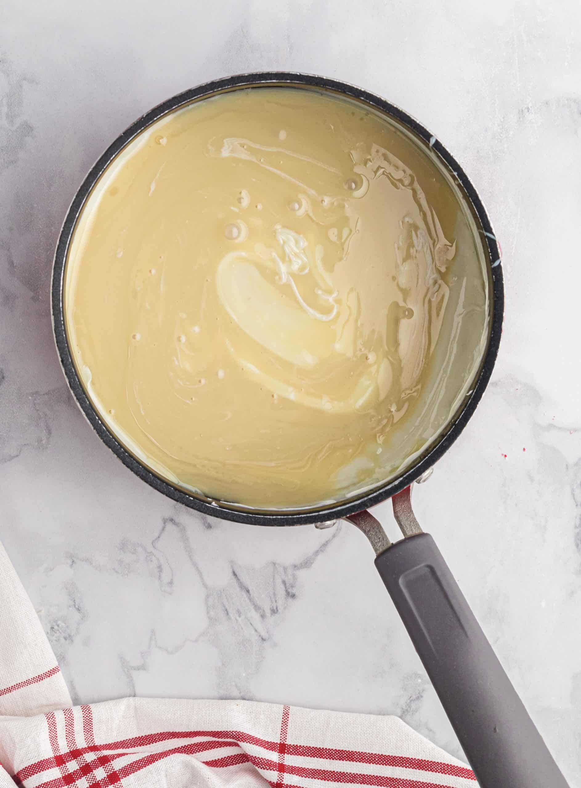 sweetened condensed milk added to melted white chocolate in a sauce pan.