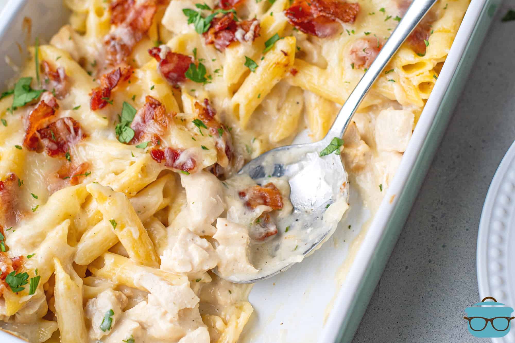fully baked chicken bacon ranch casserole in a baking dish with a silver serving spoon.