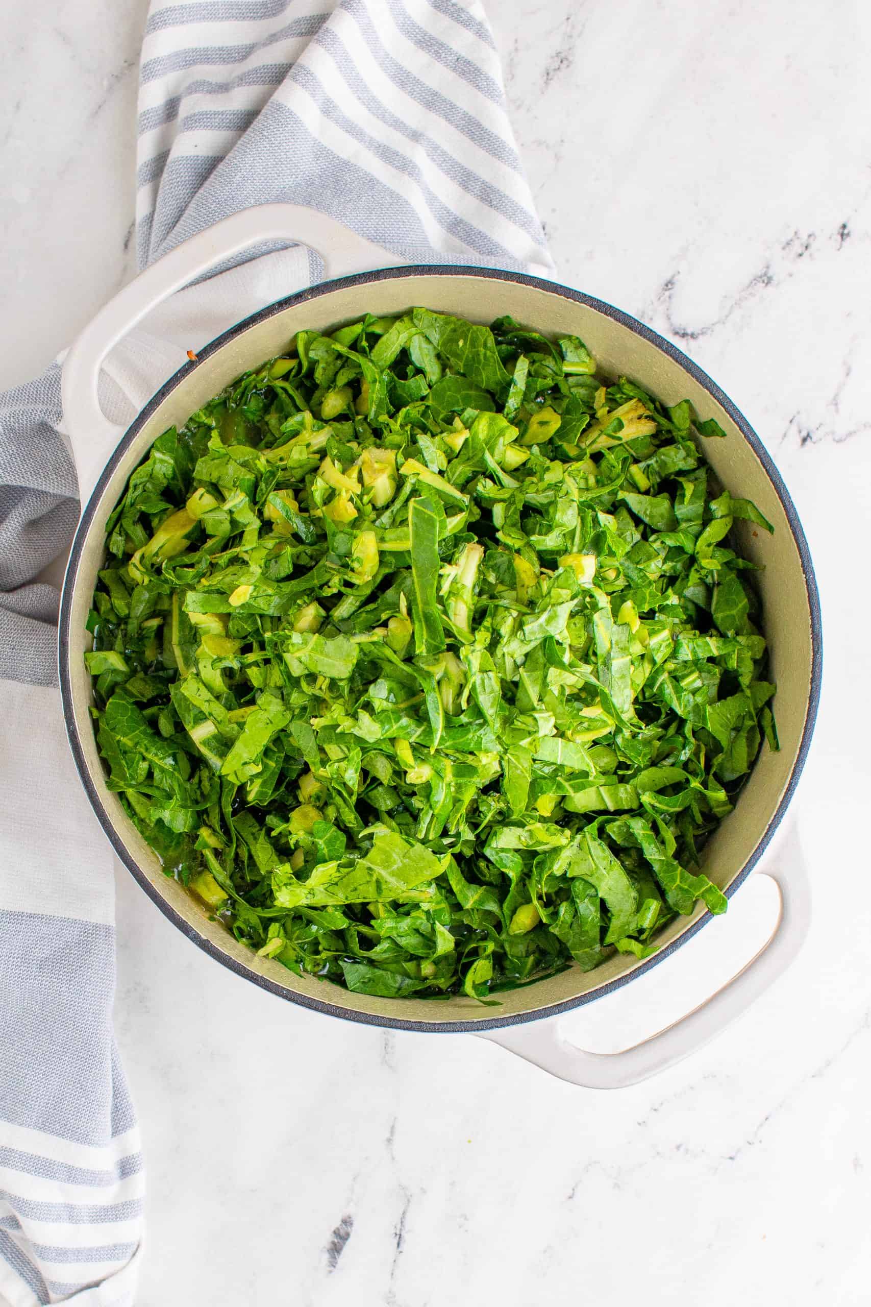 shredded collared greens in a white dutch oven pot shown on a marble surface 