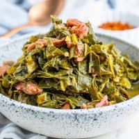 Collard Greens with ham in a speckled white and blue bowls with a copper spoon in the background