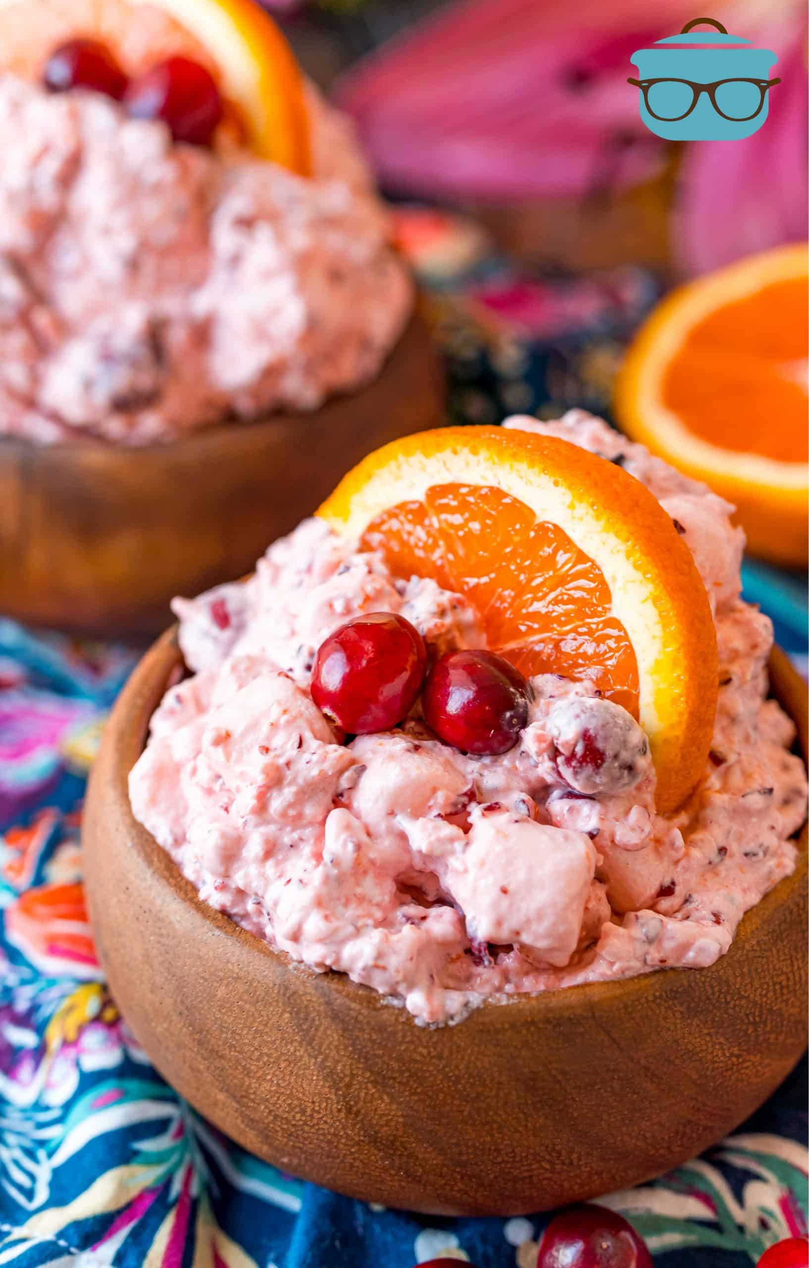 Cranberry Orange Fluff shown in small wood bowls and topped with a slice of orange and fresh cranberry.