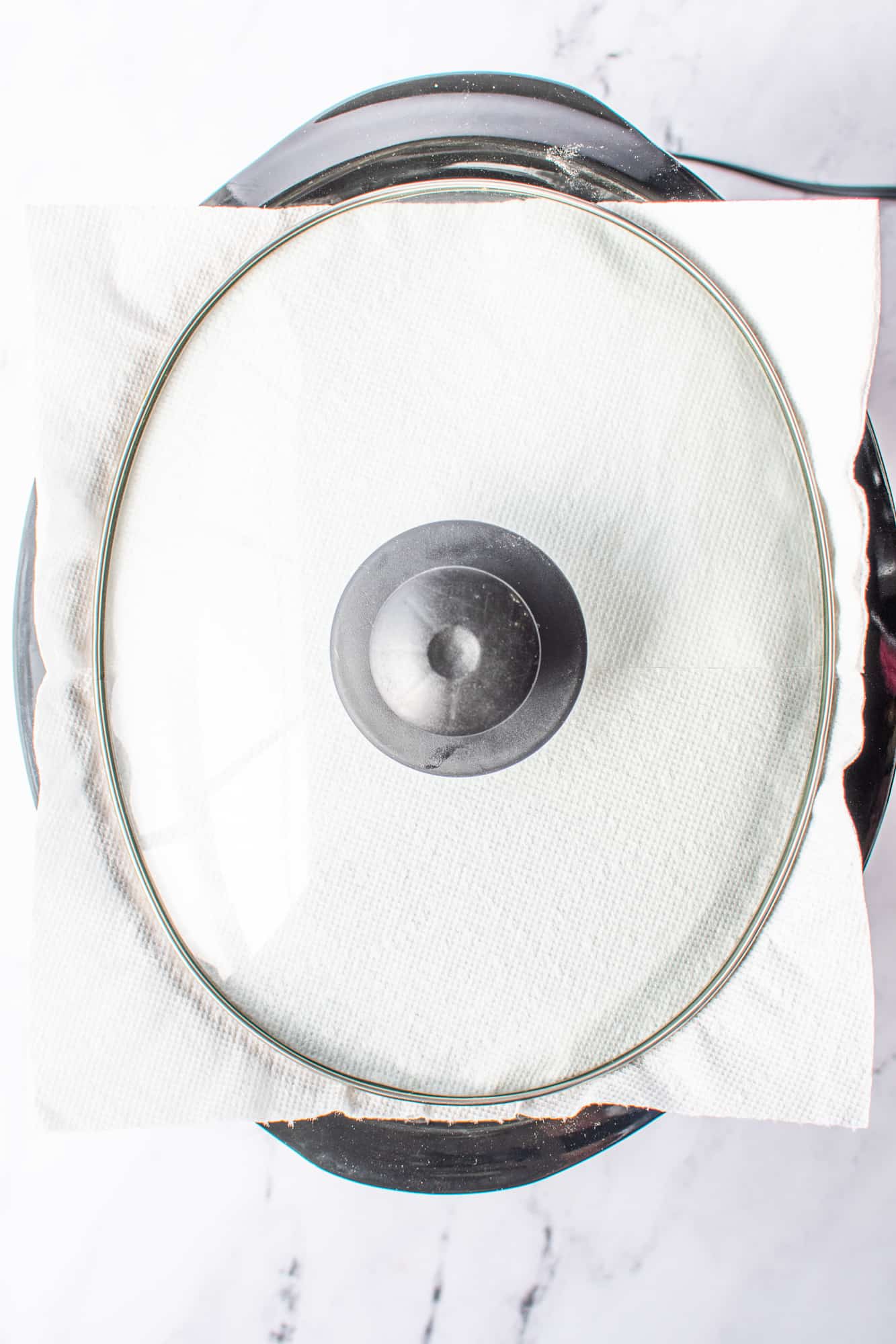a covered slow cooker shown with a paper towel underneath the lid