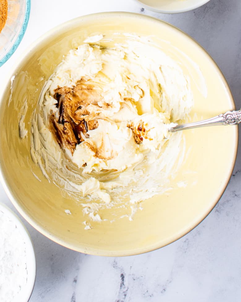 powdered sugar, cream cheese and maple flavoring mixed together in a light yellow bowl with a spoon