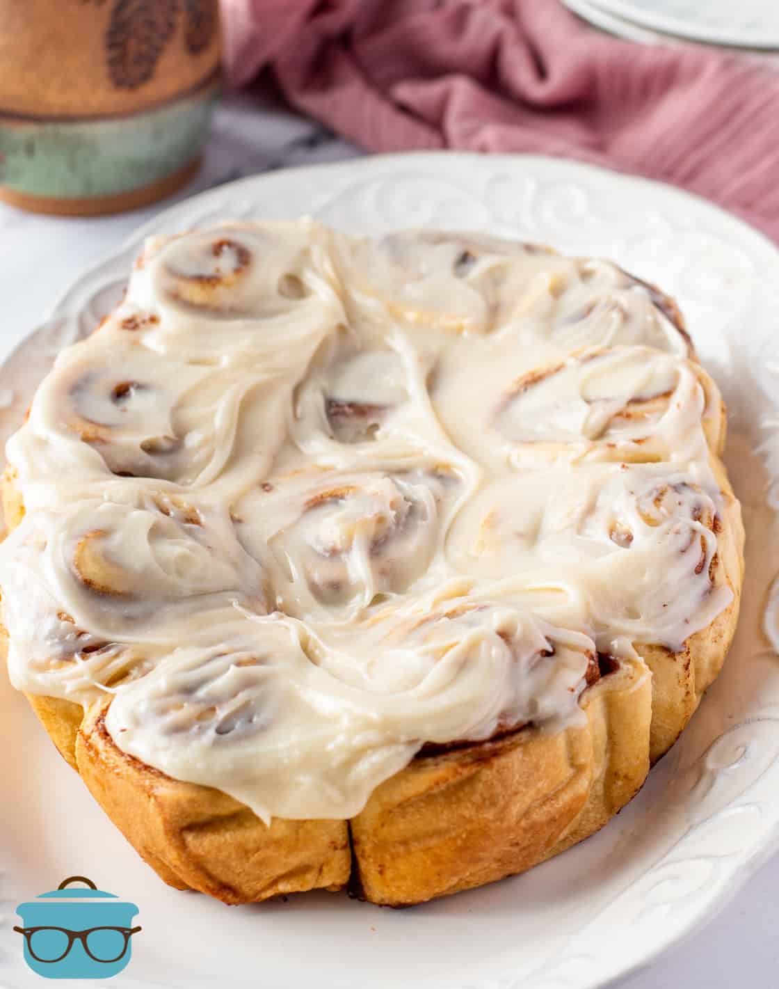 fully baked cinnamon rolls topped with cream cheese icing, shown on a white oval platter