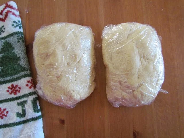 two sugar cookie dough balls wrapped in plastic wrap on a wooden surface