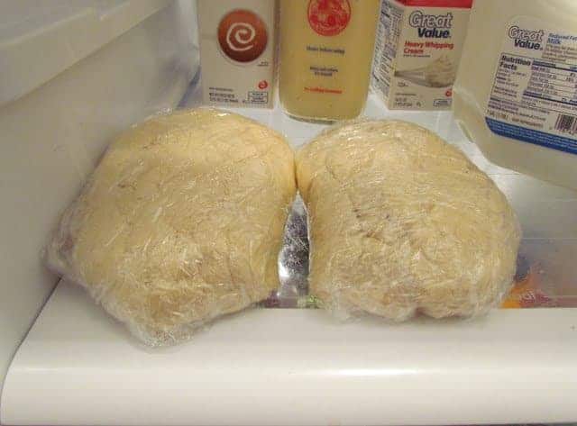 sugar cookie dough balls wrapped in plastic shown on a shelf in the refrigerator