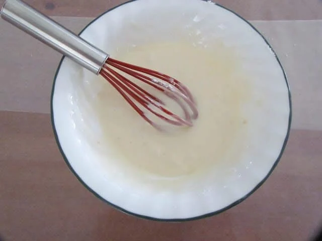 powdered sugar icing in a white bowl with a red whisk inside