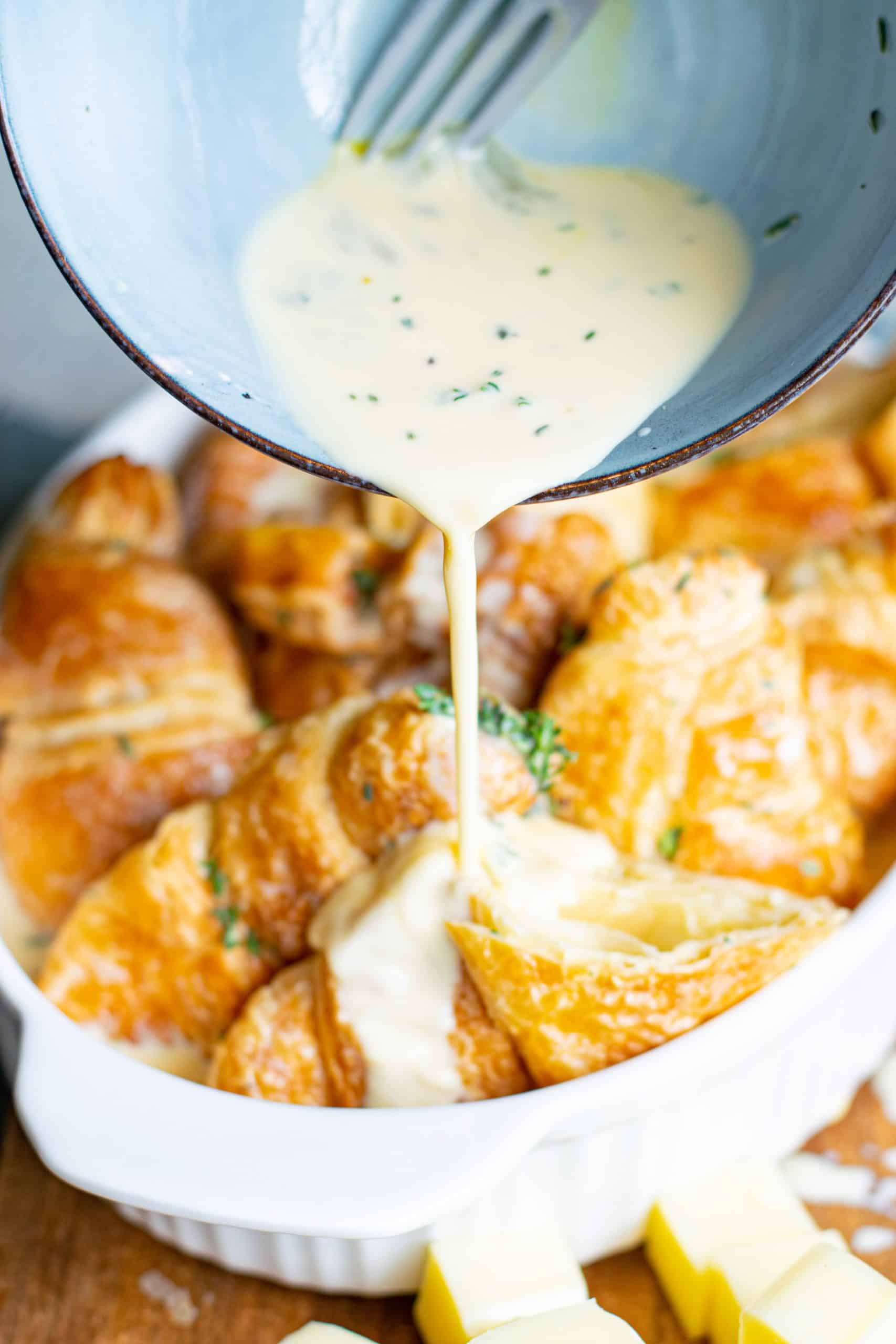 pour egg and cream mixture over croissants in a white oval baking dish.