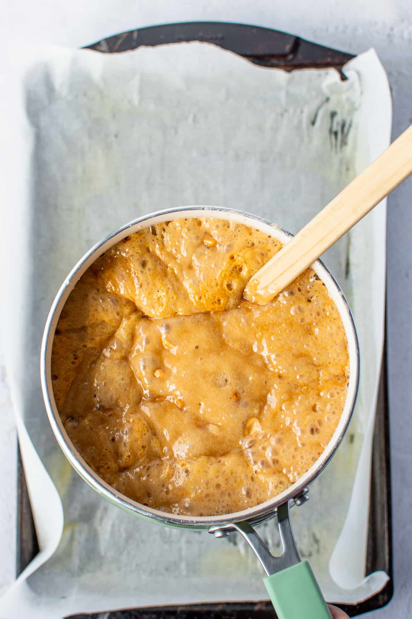 boiling peanut brittle in a liquid state in a sauce pan with a wooden spoon.