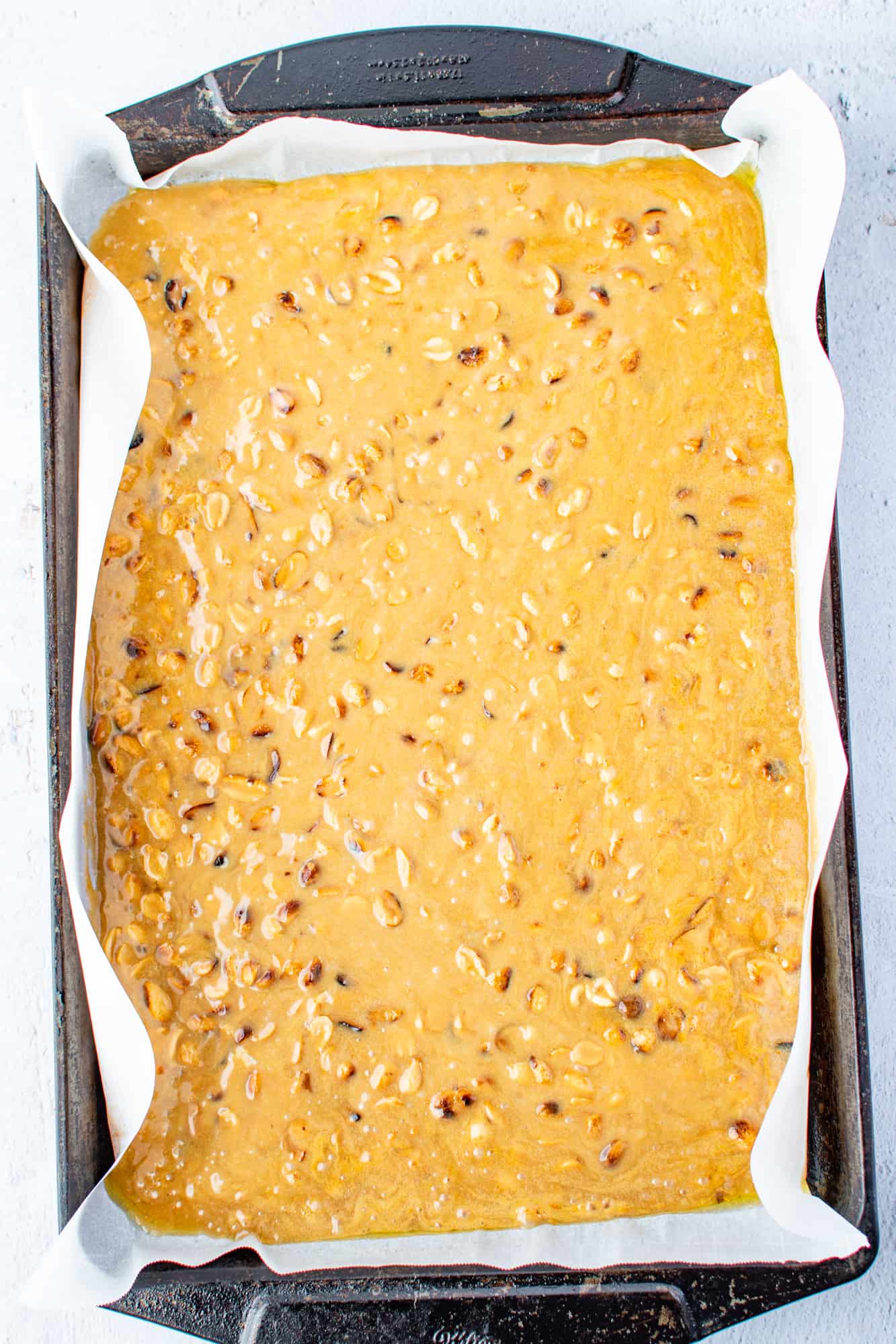 liquid peanut brittle shown after it has been poured onto a cookie sheet lined with parchment paper.