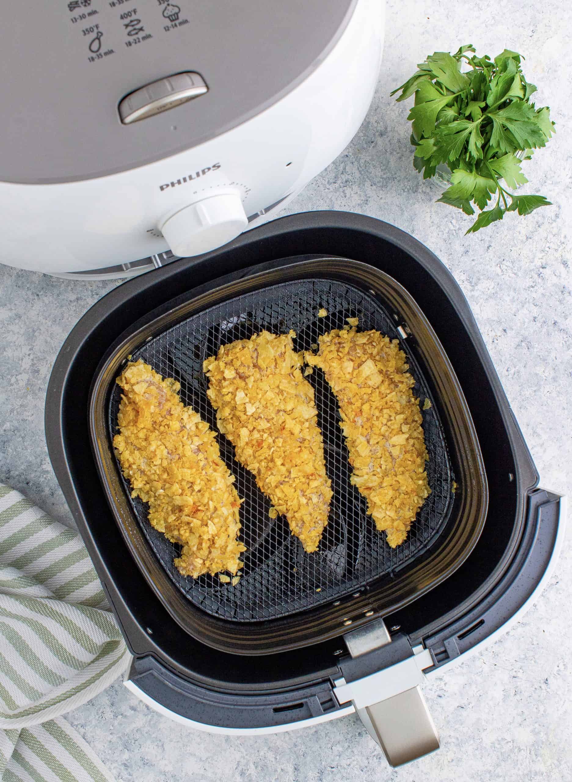 raw, coated chicken tenders in the bottom of a black air fryer basket.