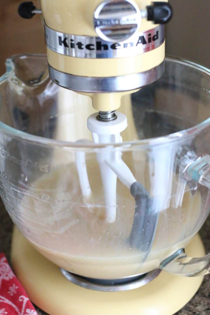 eggs, oil, milk, cooled coffee and vanilla extract combined in a clear mixing bowl in a yellow stand mixer.