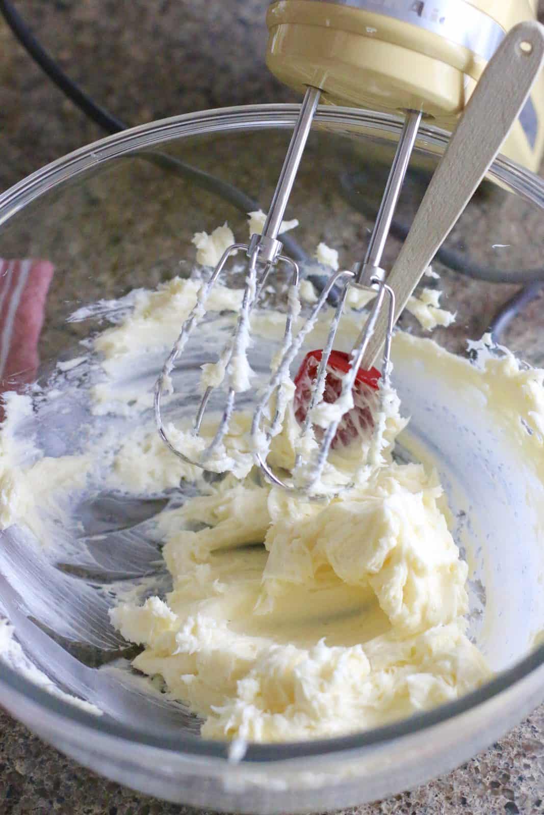 butter mixed in a clear glass mixing bowl, hand mixer shown in bowl.