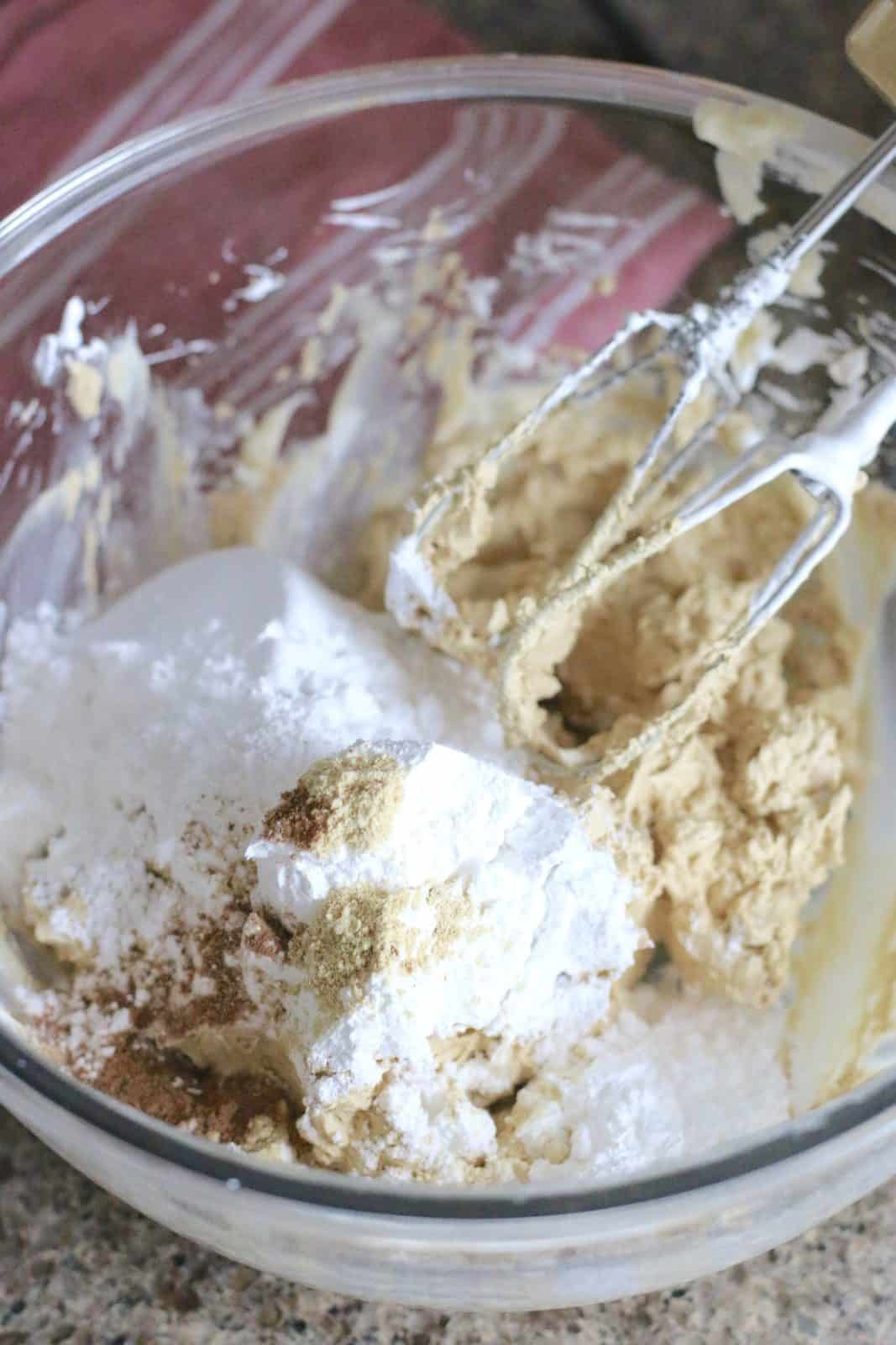 powdered sugar and spices added to molasses butter mixture in a clear bowl.