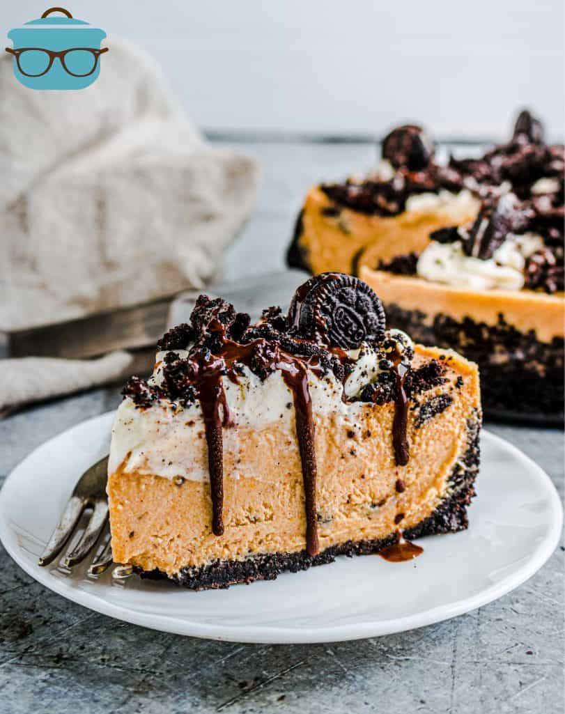 slice of Oreo Pumpkin Cheesecake on a small white plate with the rest of the pie in the background