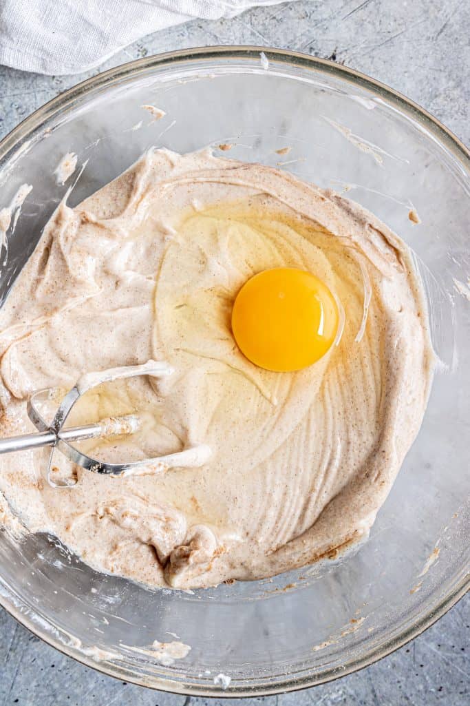 egg shown on top of pumpkin cheesecake mixture in a clear bowl with an electric mixer