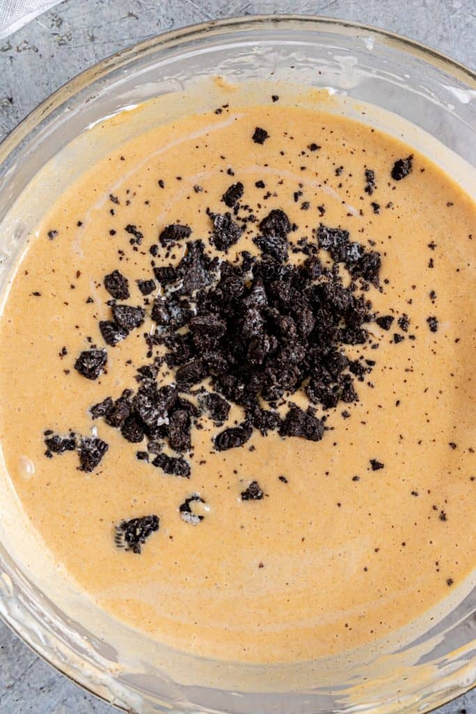 crushed Oreo cookies added to pumpkin cheesecake batter in a clear bowl