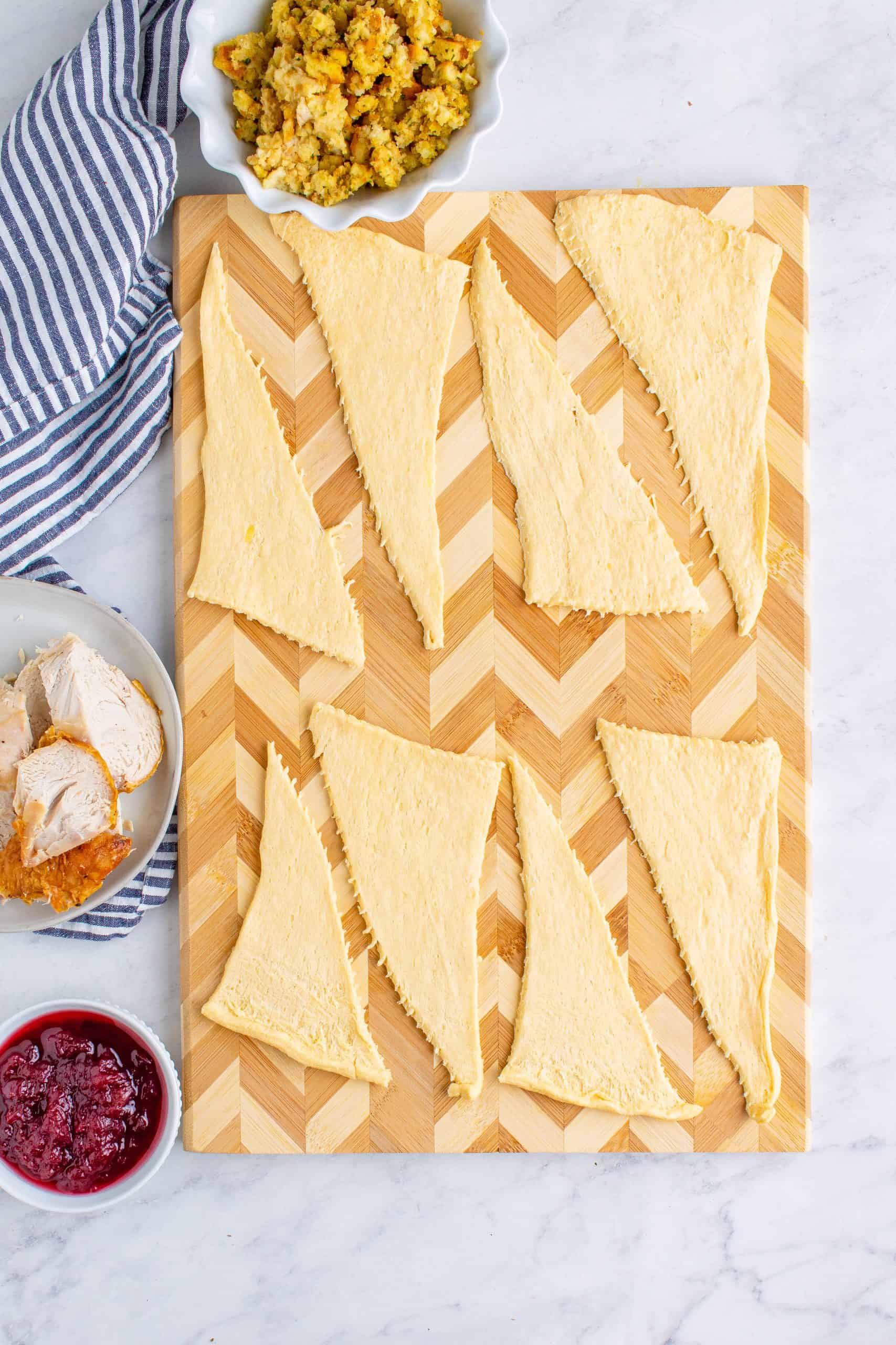 crescent roll triangles laid out on a wooden cutting board.