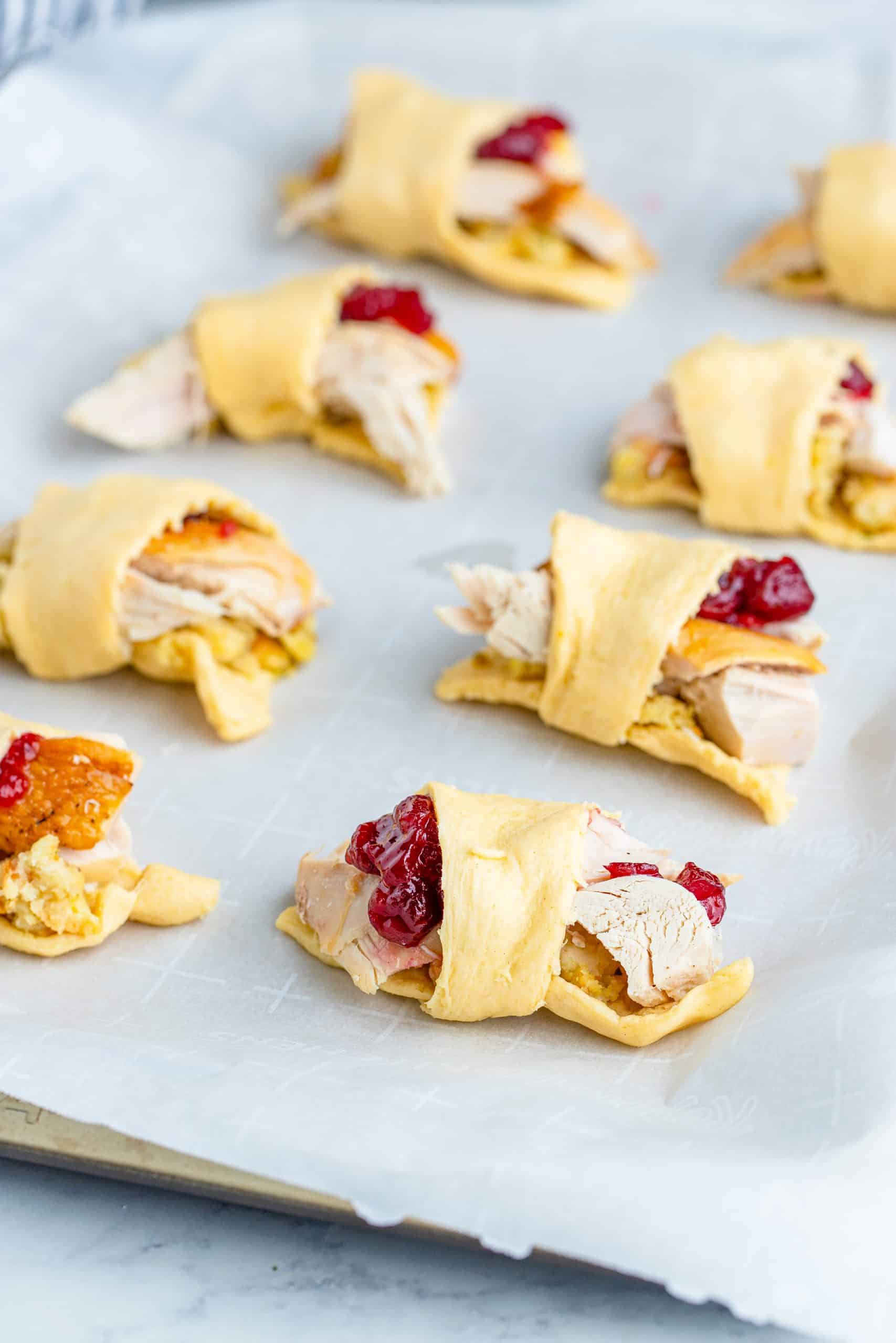 Thanksgiving leftovers rolled up into crescent roll dough on parchment paper lined baking sheet.