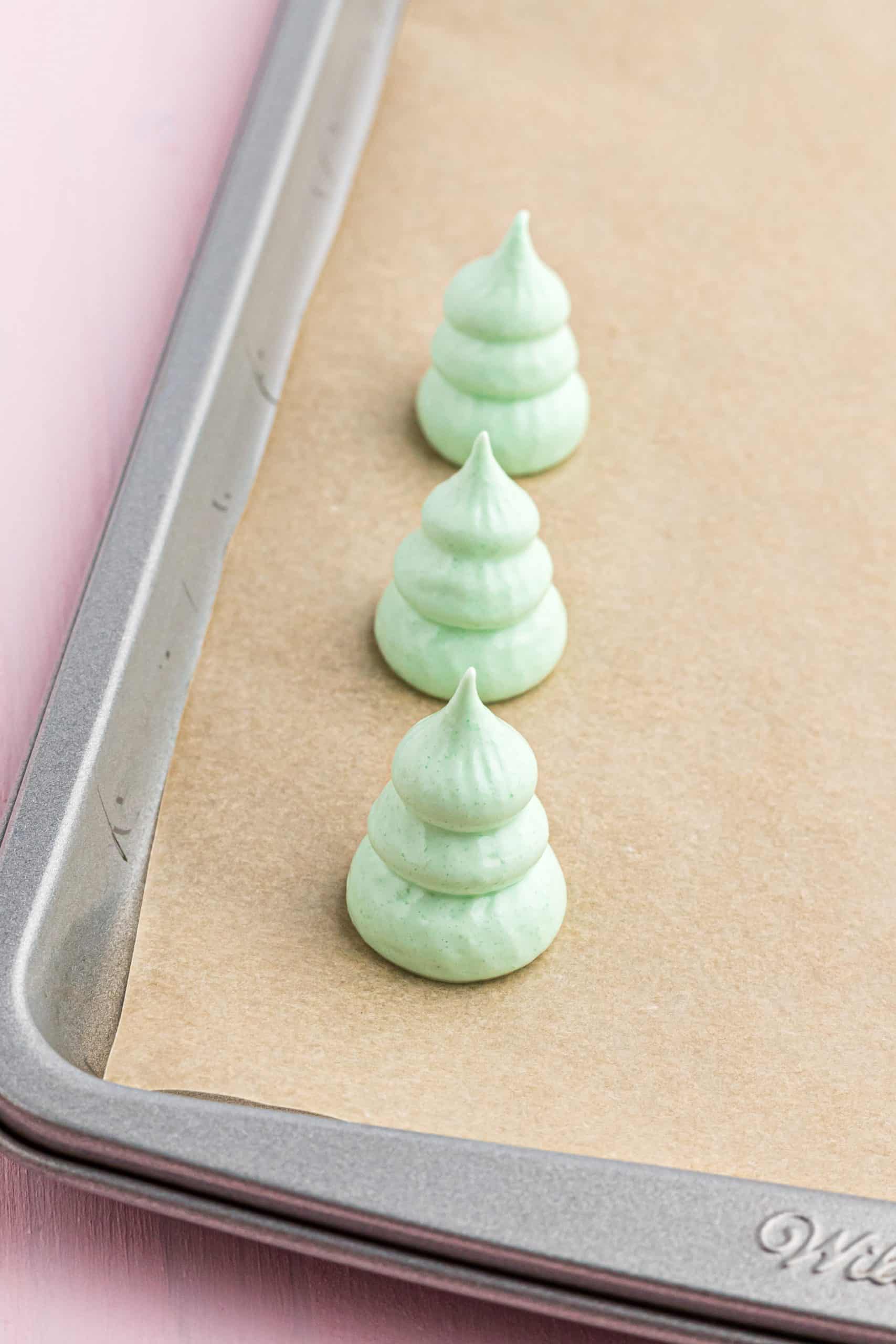 meringue Christmas trees just after they have been "piped" onto the brown parchment paper on a baking sheet.
