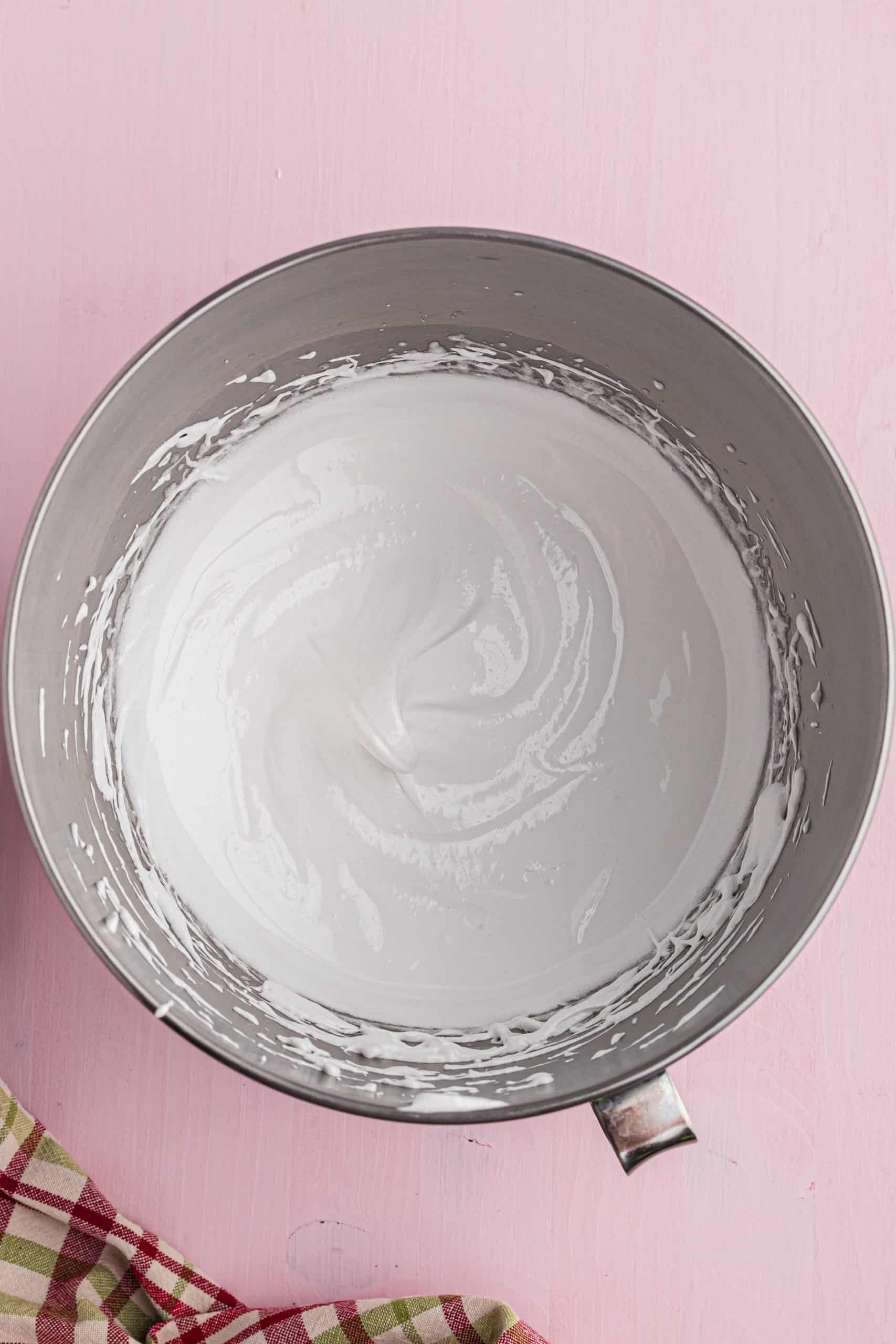 creamy and thick egg whites with sugar in a stainless steel mixing bowl.