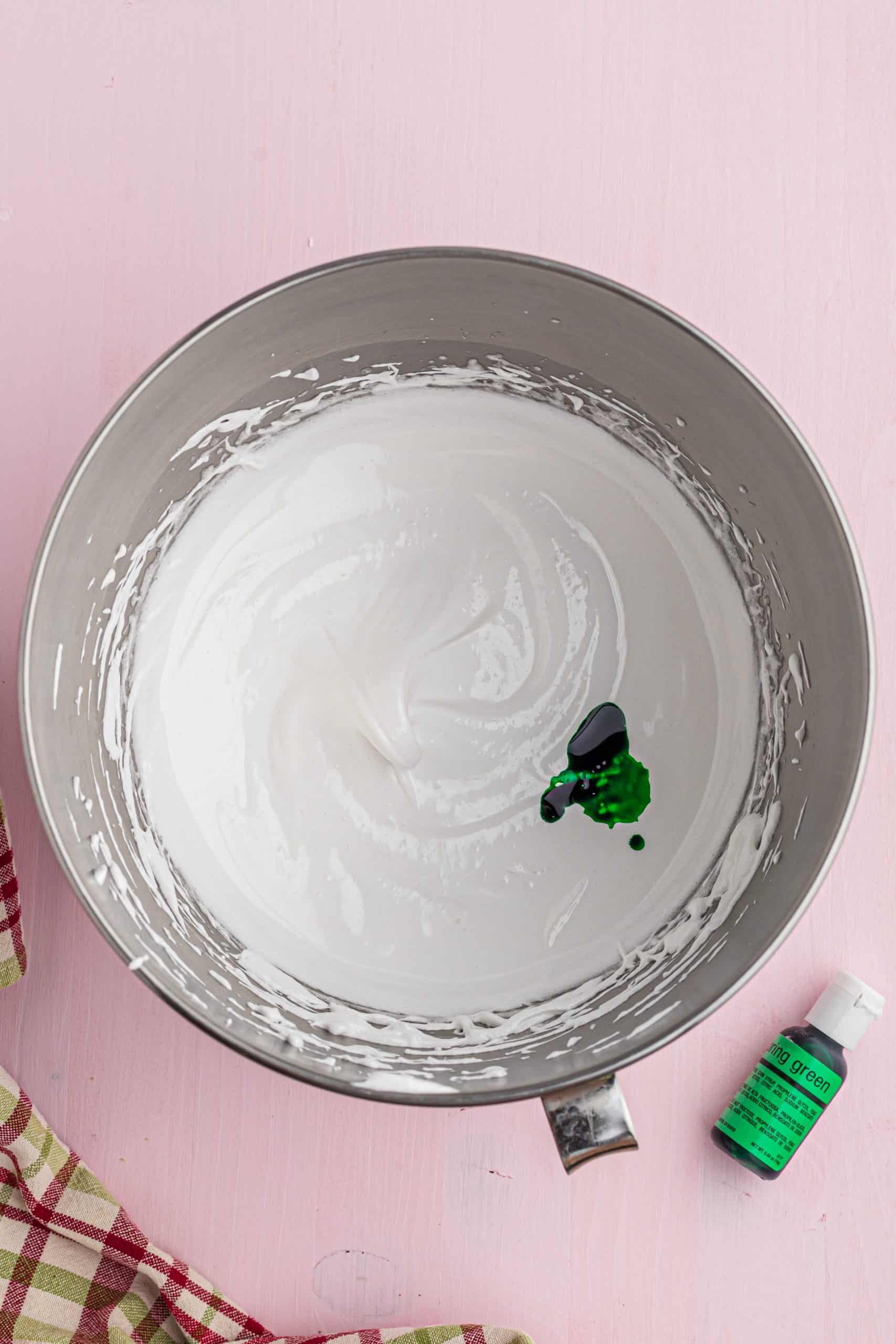 green food coloring in meringue batter in a mixing bowl.
