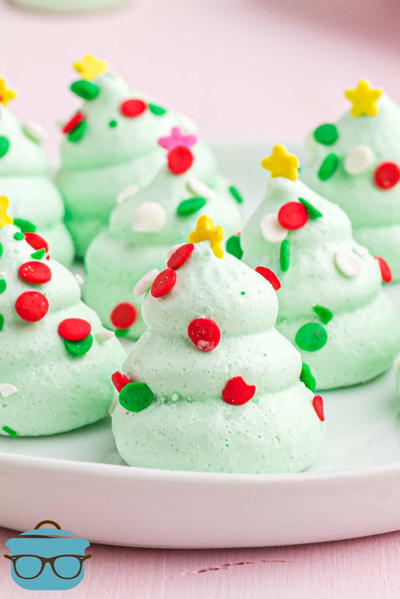 green Christmas tree shaped meringue cookies shown on a small white plate on a pink background.