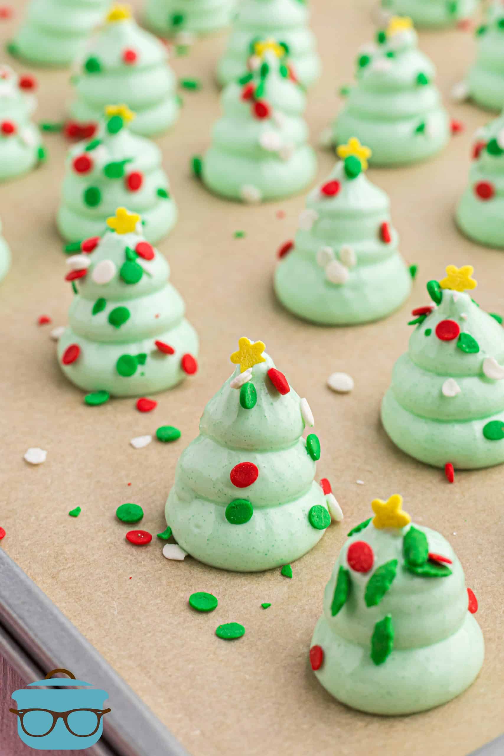 green meringue Christmas trees with sprinkles on brown parchment paper.